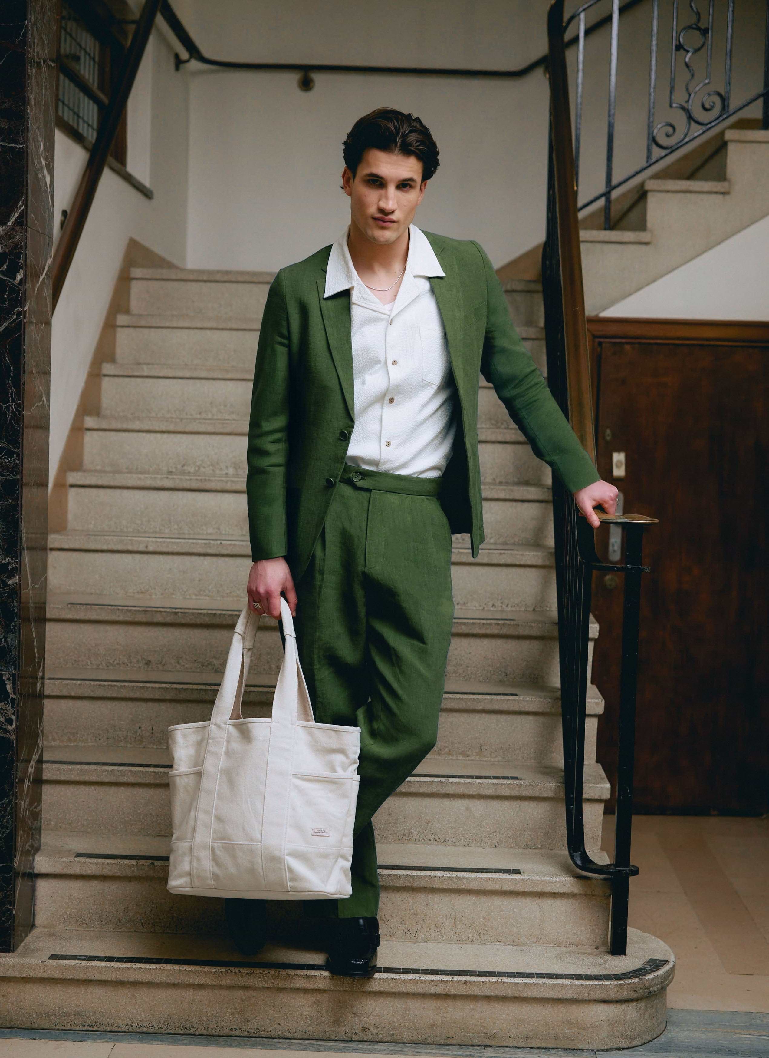 A model on a staircase wearing the Percival Linen Blazer in Forest Green with matching trousers and a white shirt.