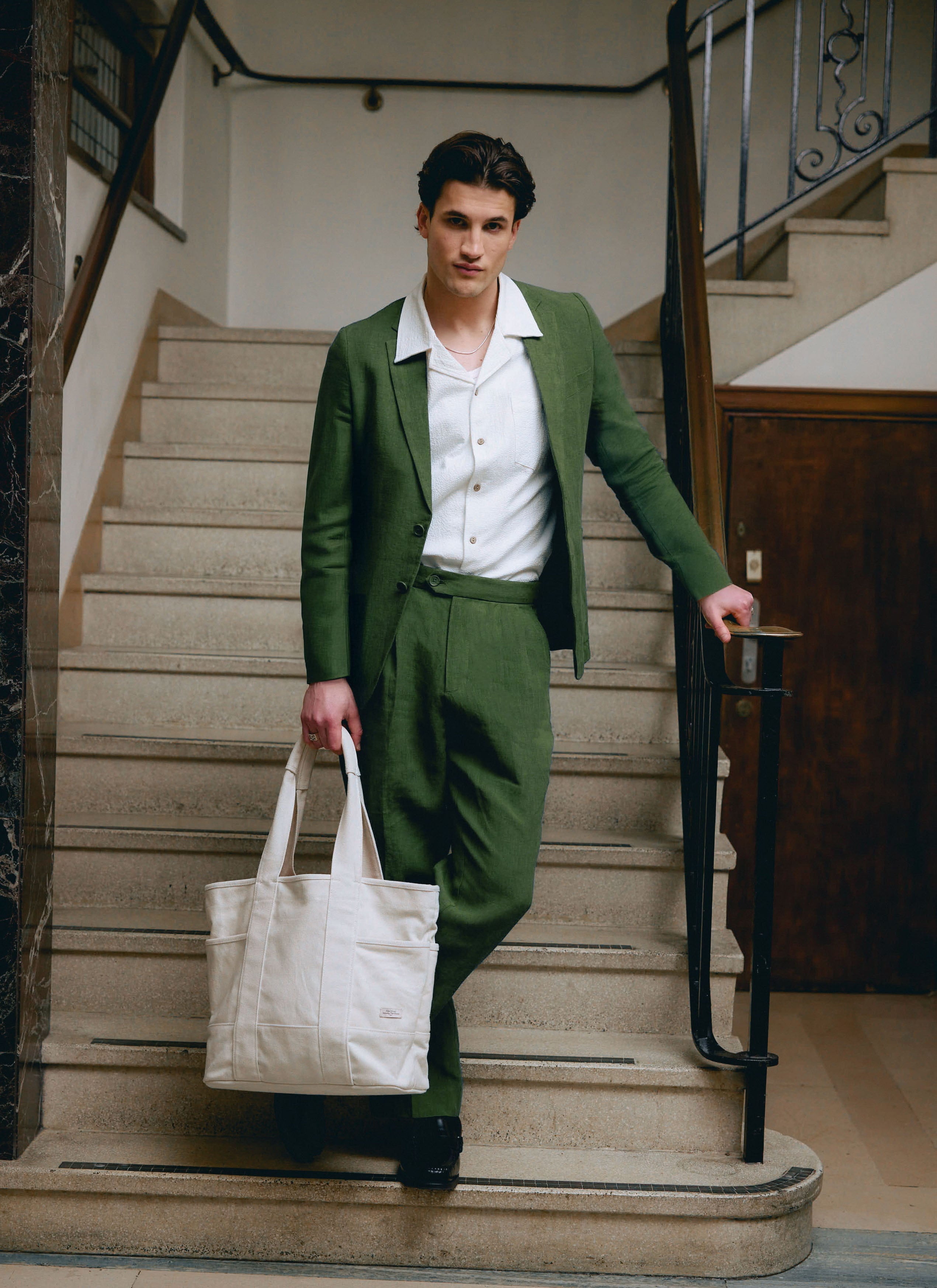 A model on a staircase wearing the Percival Linen Blazer in Forest Green with matching trousers and a white shirt.