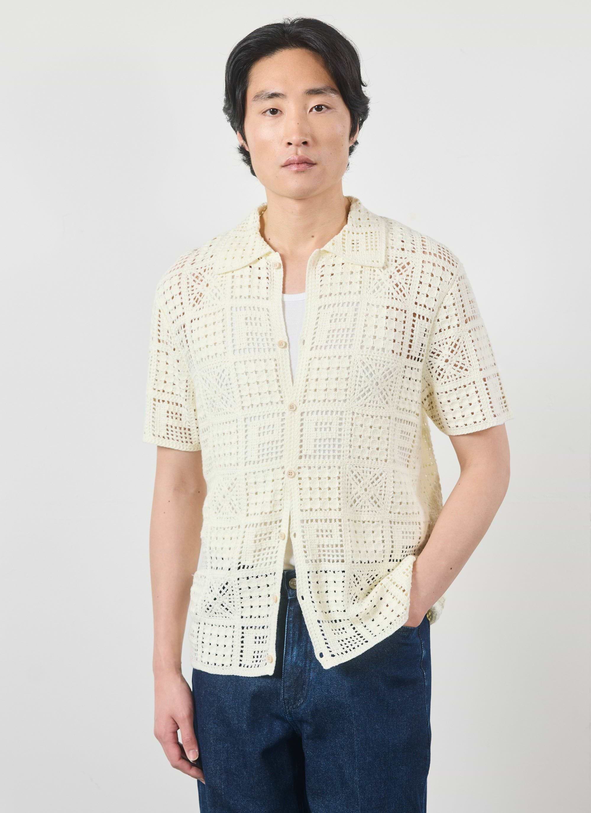 The Percival Crochet Groundsman Shirt in ecru, a short-sleeve cotton knit, shown on a model with a white vest and jeans.