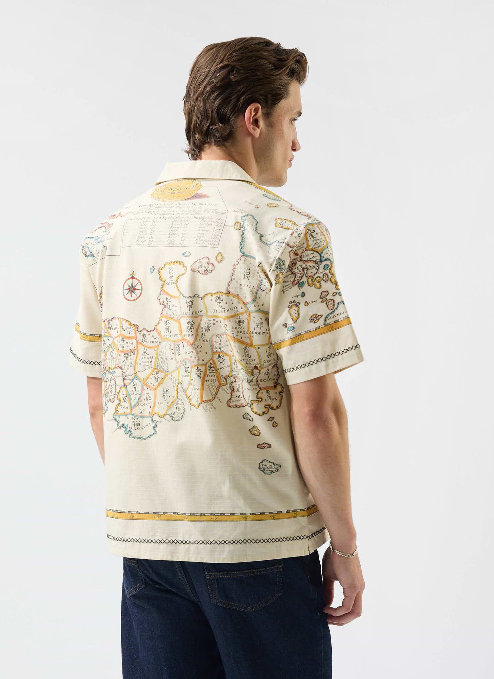 A model seen from behind wearing the Percival Ex Libris Cuban shirt in ecru, showing the detailed map artwork.