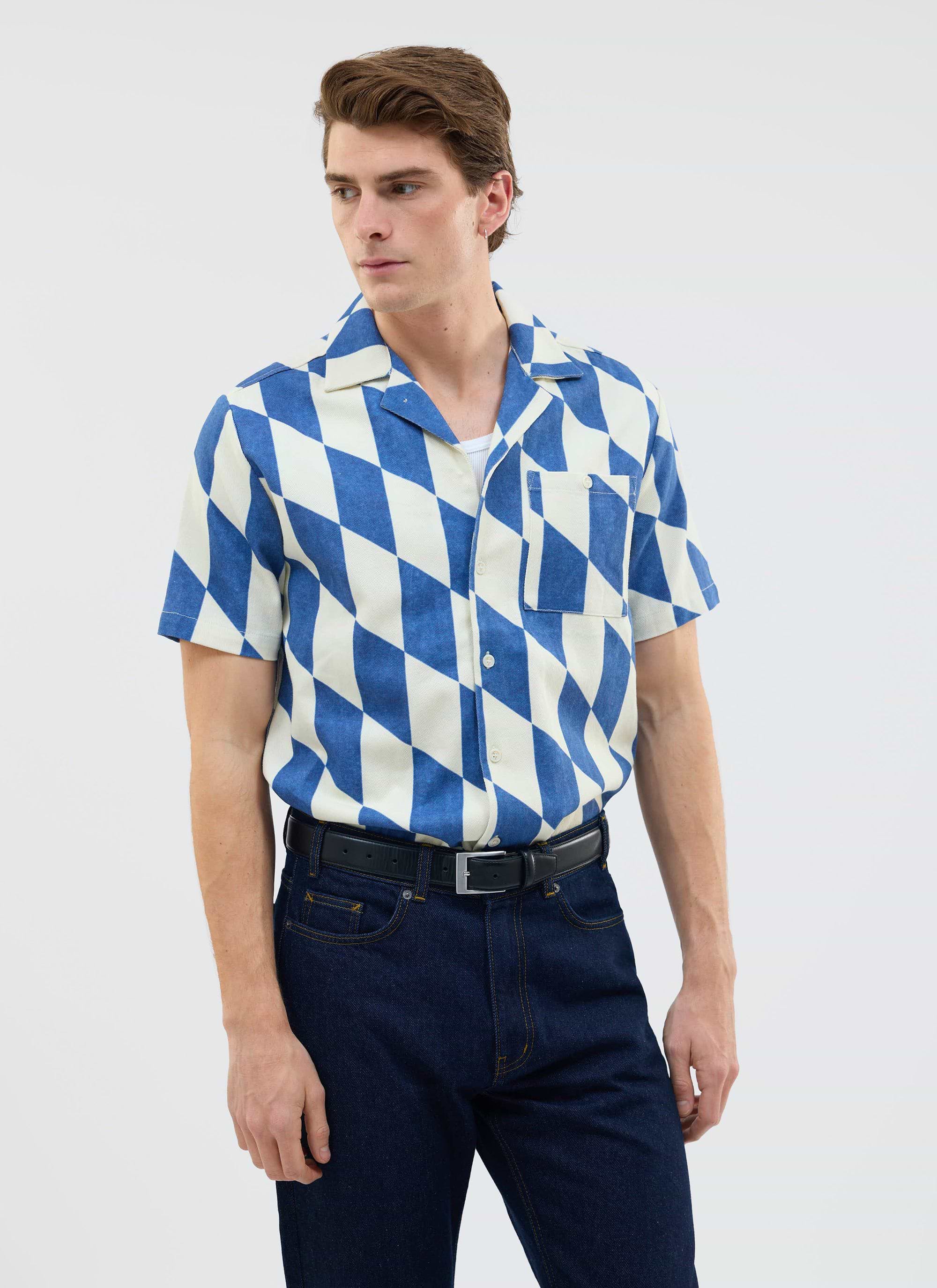 A model wears the Percival Market Diamond Cuban Shirt in ecru and navy, which has a diamond pattern, with dark denim jeans.