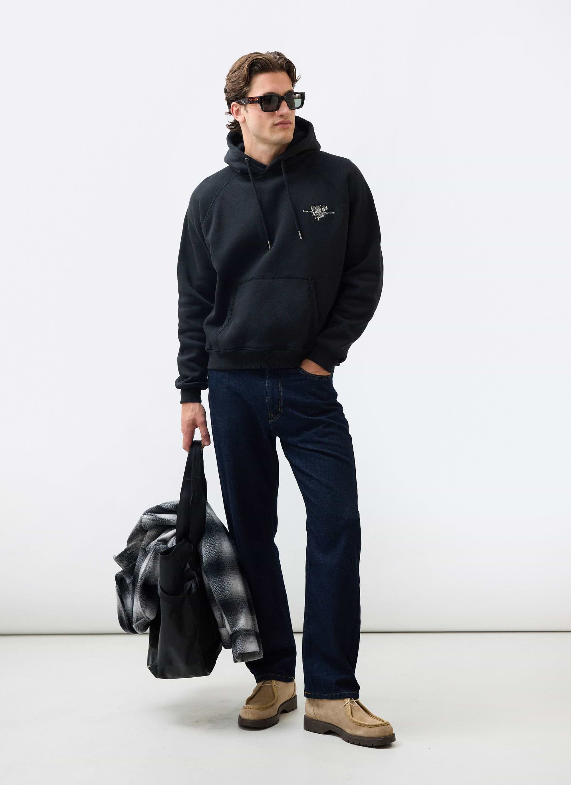A model wearing the Percival black Heritage 90's Raglan Hoodie, sunglasses, and dark jeans against a white background.