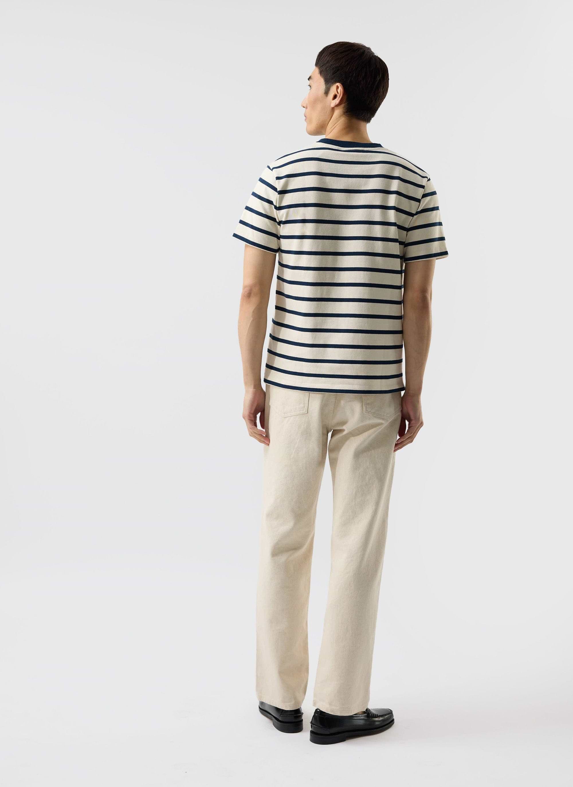 A model seen from behind wearing the Percival Breton Stripe T-shirt in ecru and navy with cream trousers and black loafers.