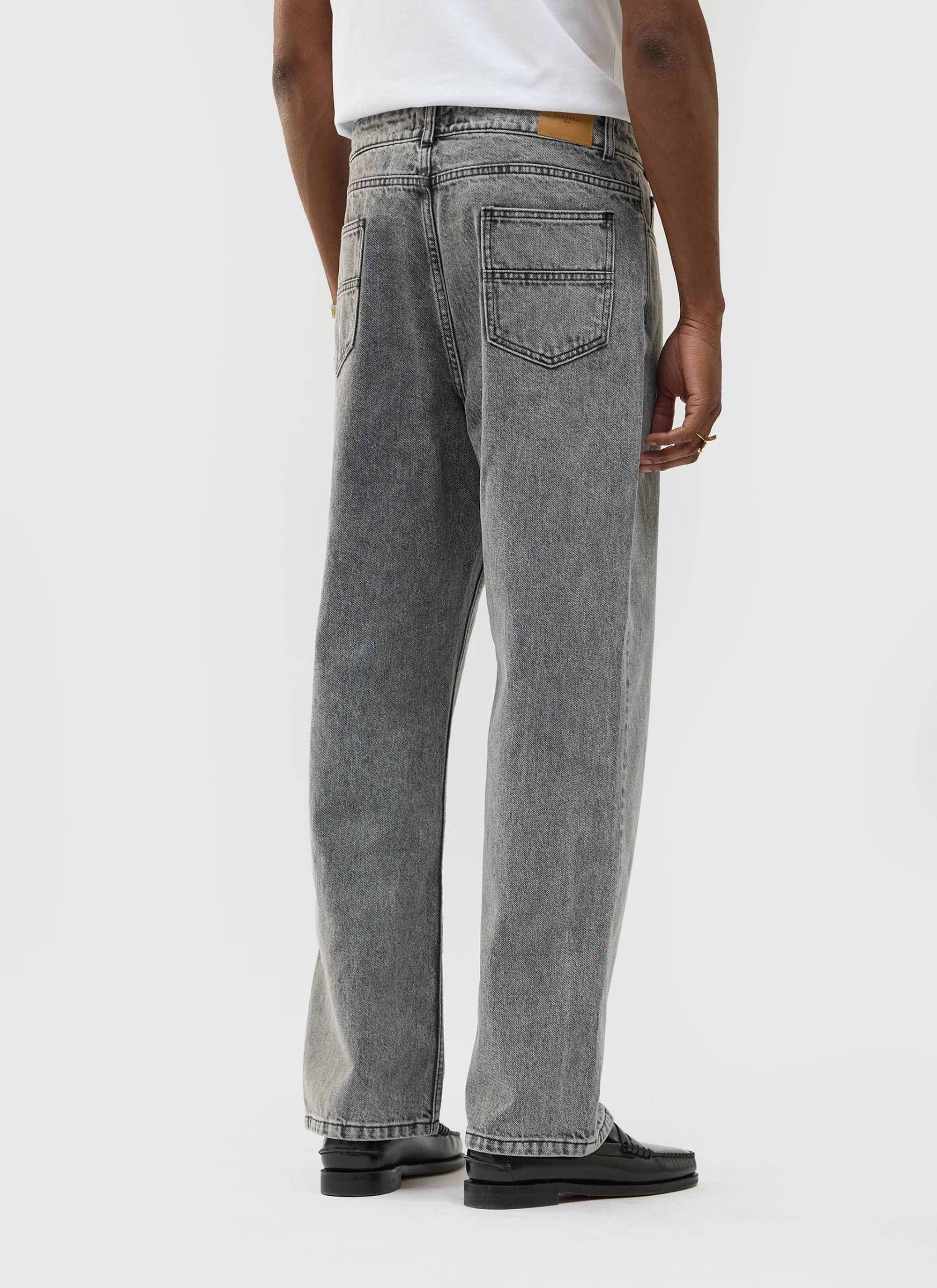 Back view of a model wearing the Percival Wide Leg Denim Jeans in a warm grey wash against a plain studio background.