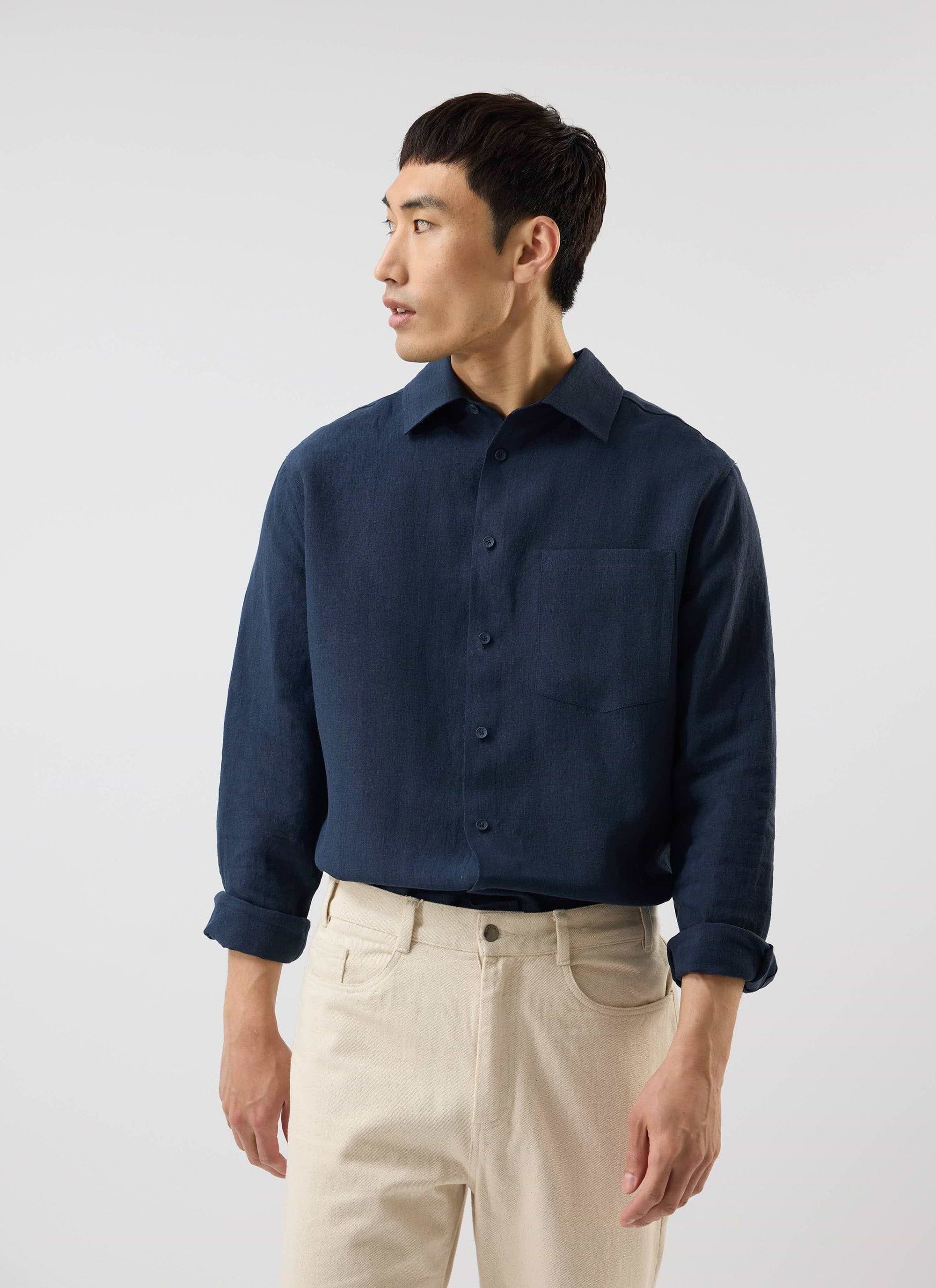 A model wears the Percival Pearce Shirt in navy linen, paired with cream trousers, in a studio.