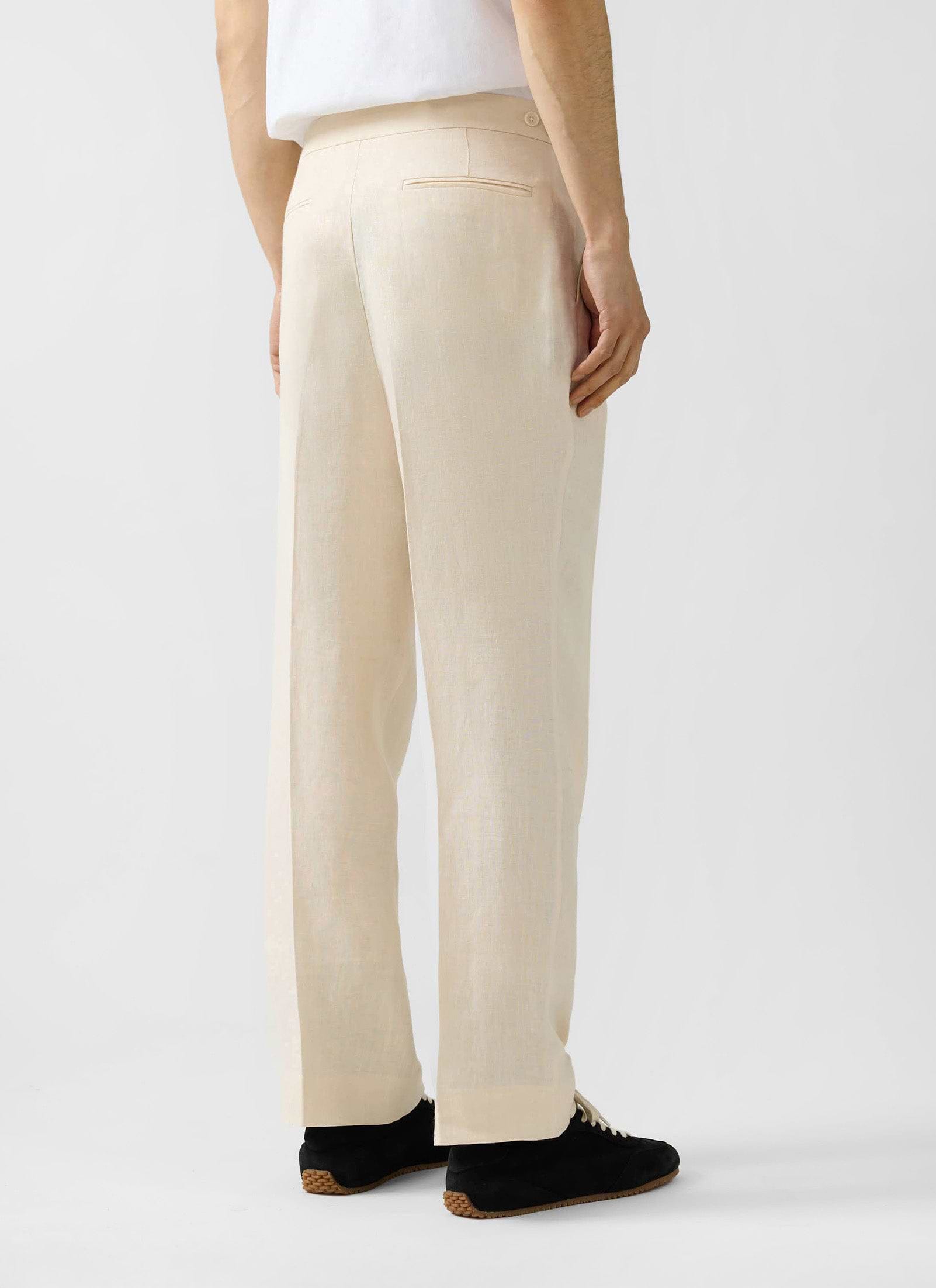 Back shot of a model wearing Percival's relaxed fit cream linen pleated tailored trousers.