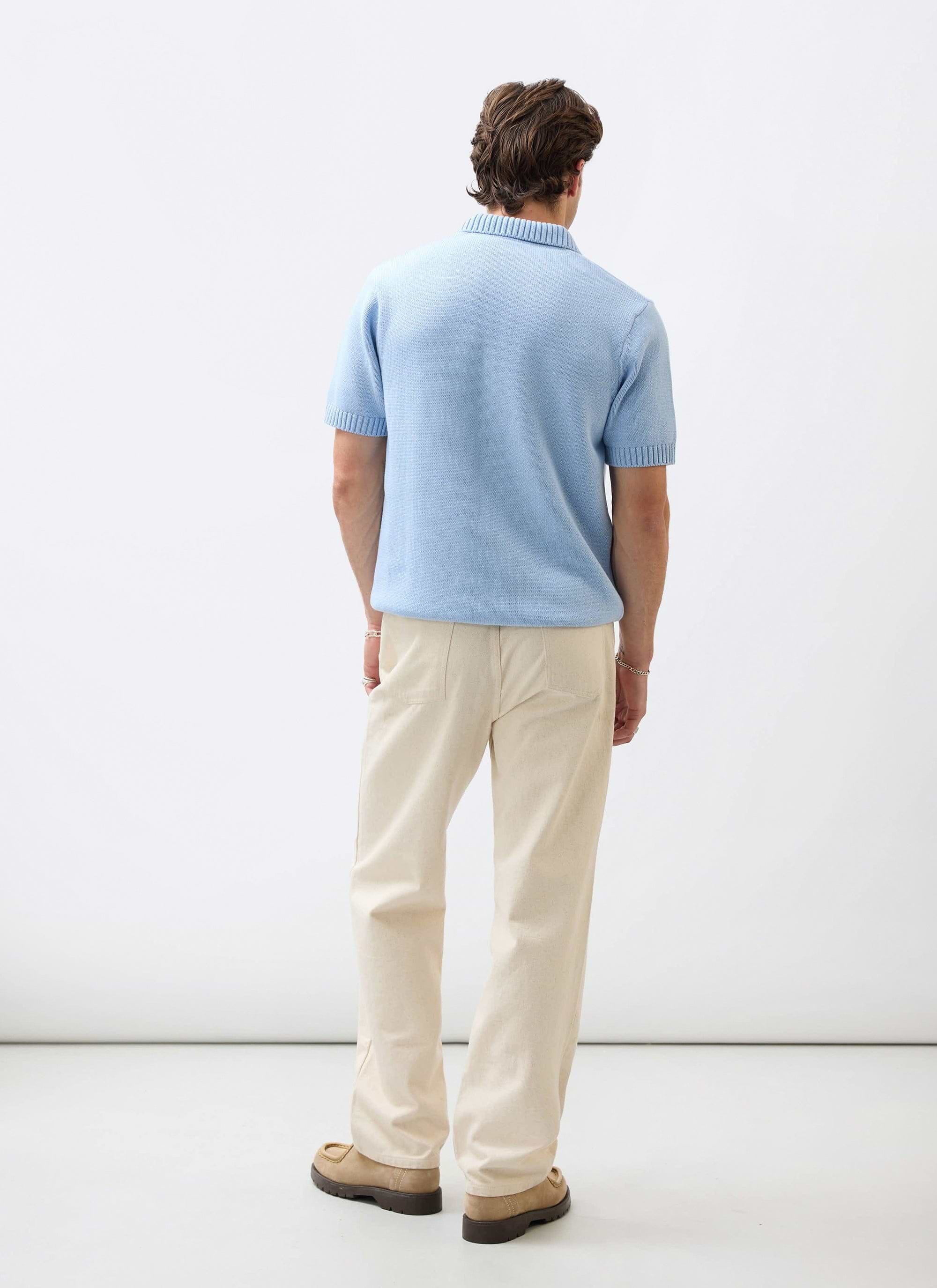 A model seen from the back wearing the Percival Verso Short Sleeve Knitted Shirt in heather blue with cream trousers.