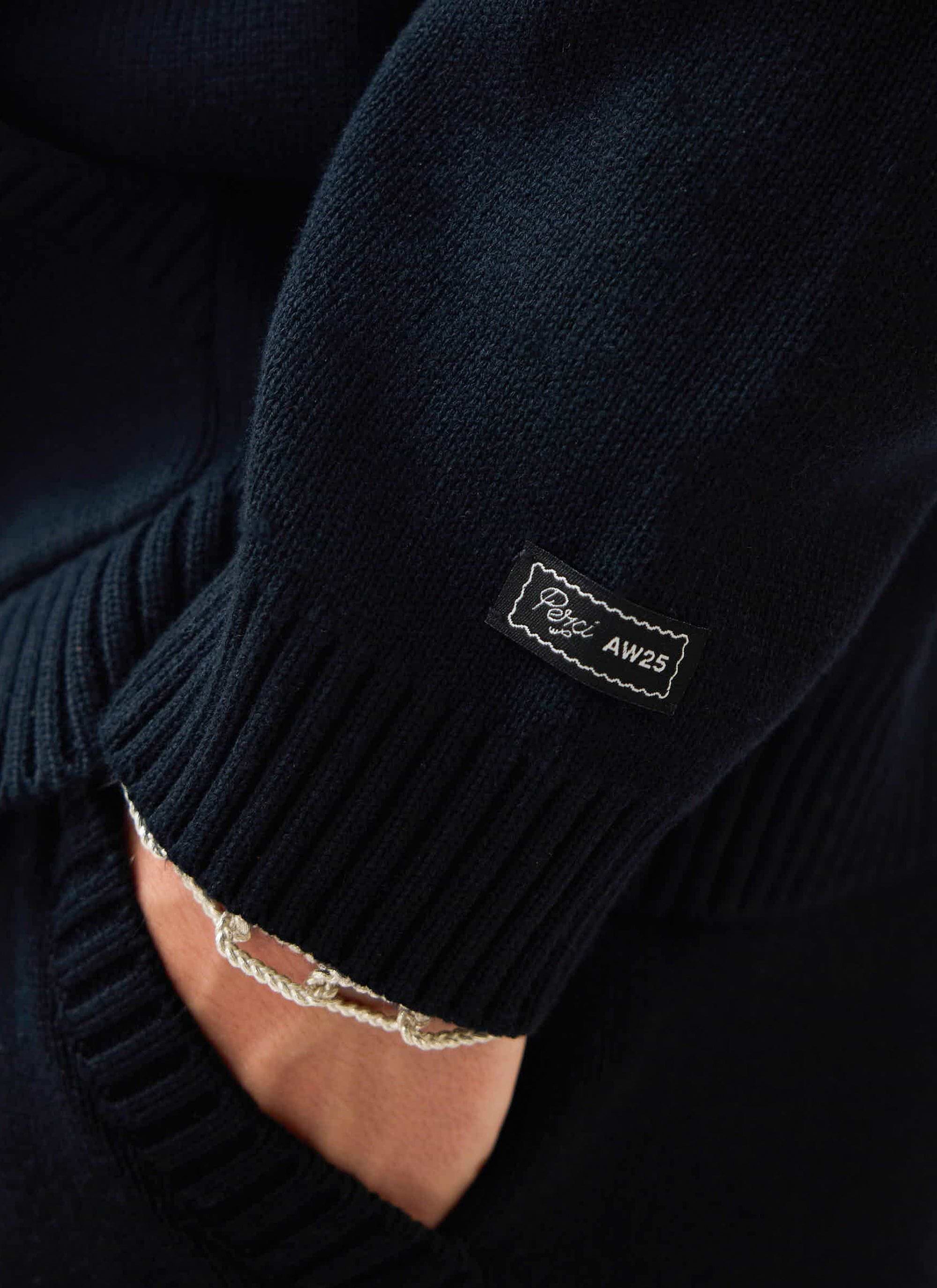 Close-up detail of the woven Percival AW25 label on the ribbed sleeve of the black cotton Chronicle Knitted Hoodie.