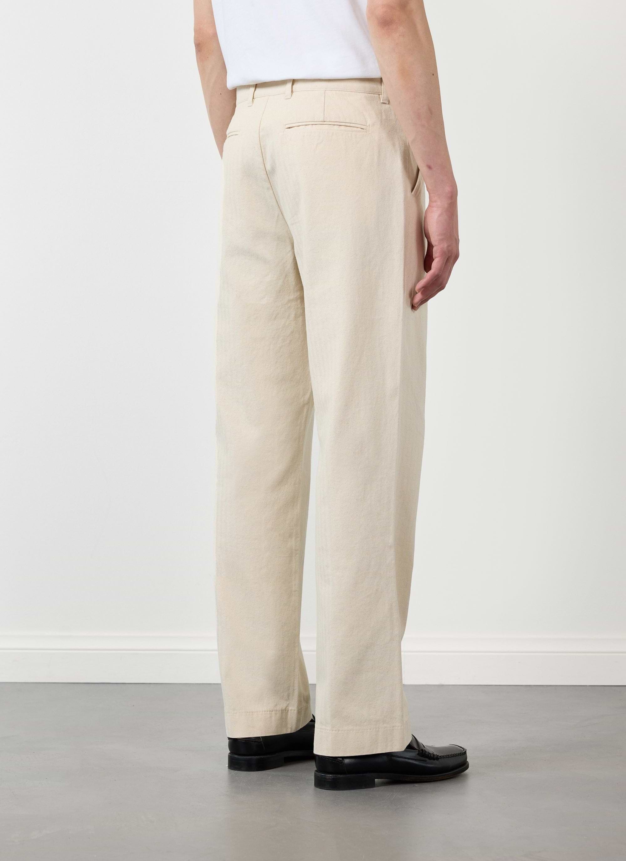Back view of a model wearing Percival's ecru cotton Program Pleated Trousers with a white t-shirt and black loafers.