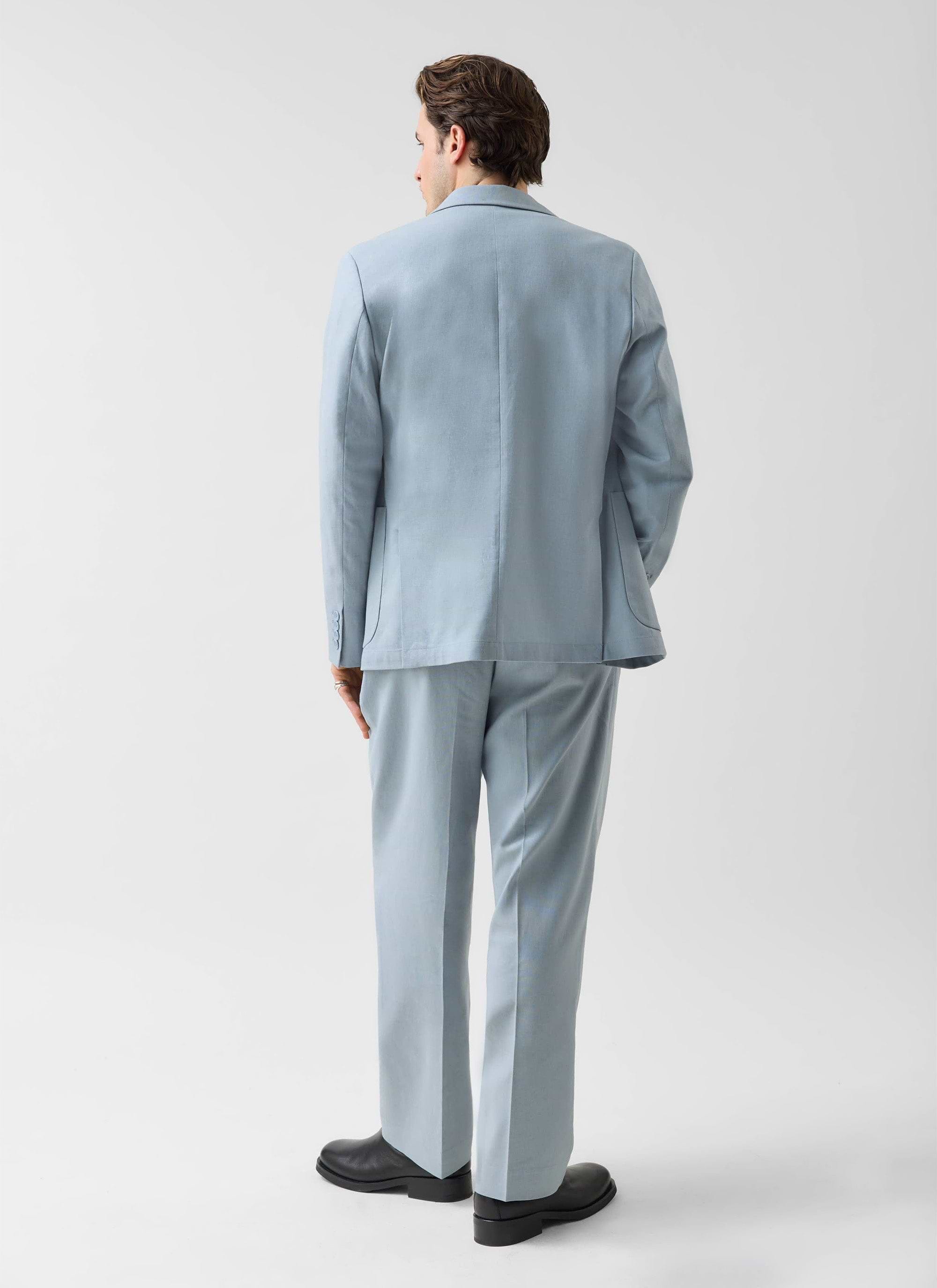 A model, seen from behind, wears the Percival Tailored Linen Blazer and matching trousers in light blue.