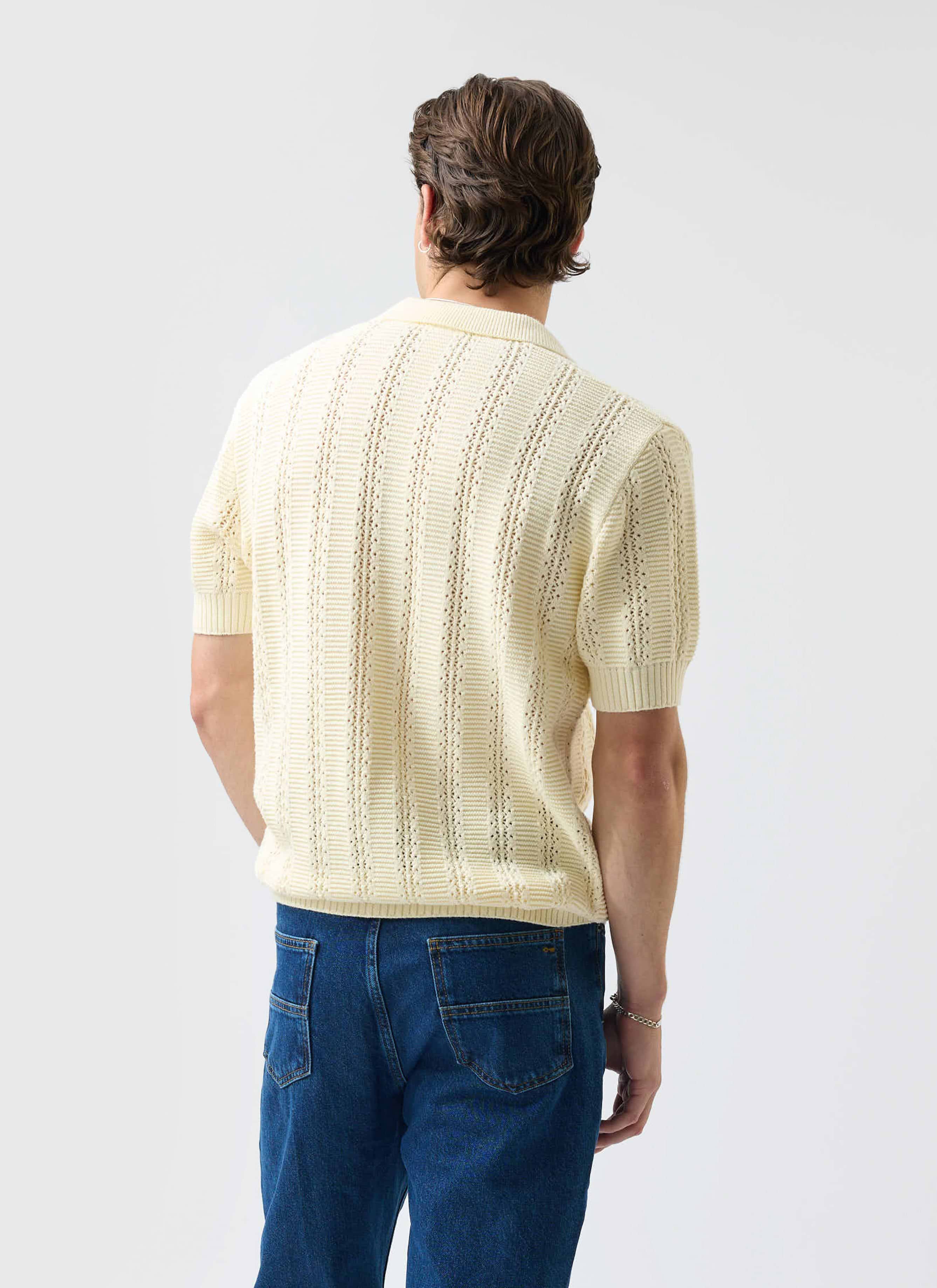 A model from the back wearing the Percival Addendum Knitted Polo Shirt in ecru cream with blue jeans.