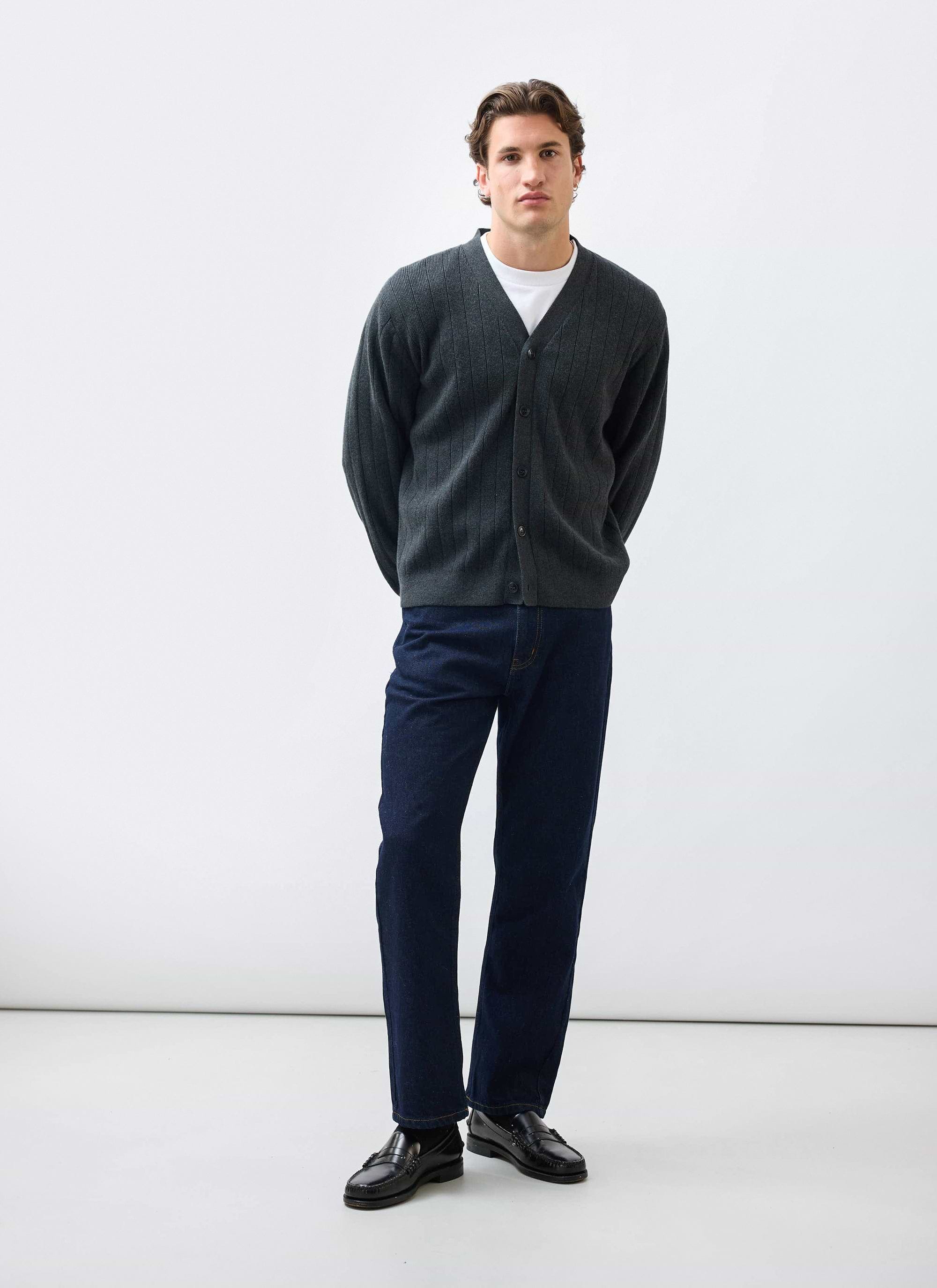A model wears the Percival Editor Cardigan in grey, styled with a white t-shirt, dark jeans and black loafers.