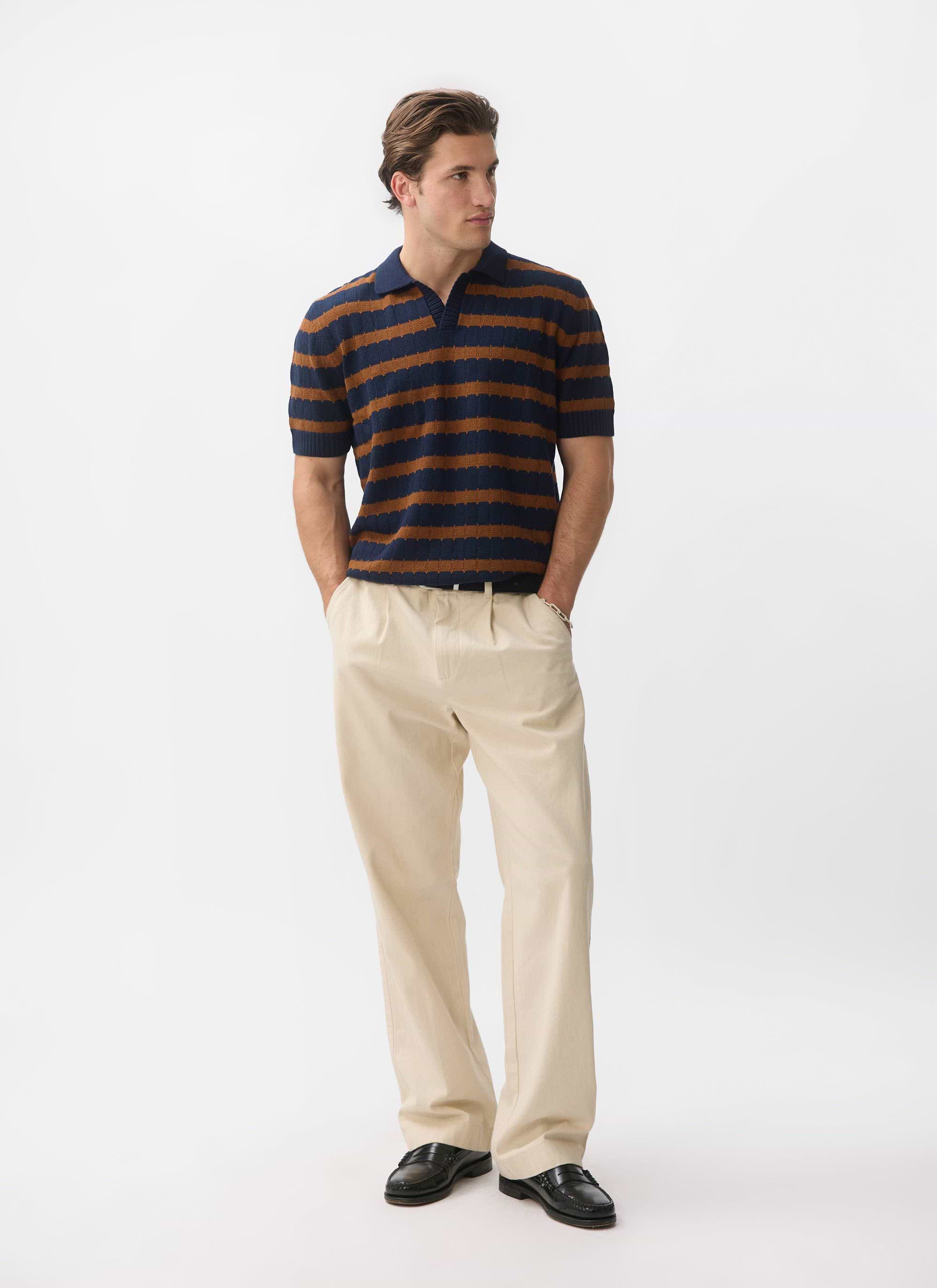 A man models the Percival Stine Knitted Polo in brown and navy, paired with cream trousers and black loafers.