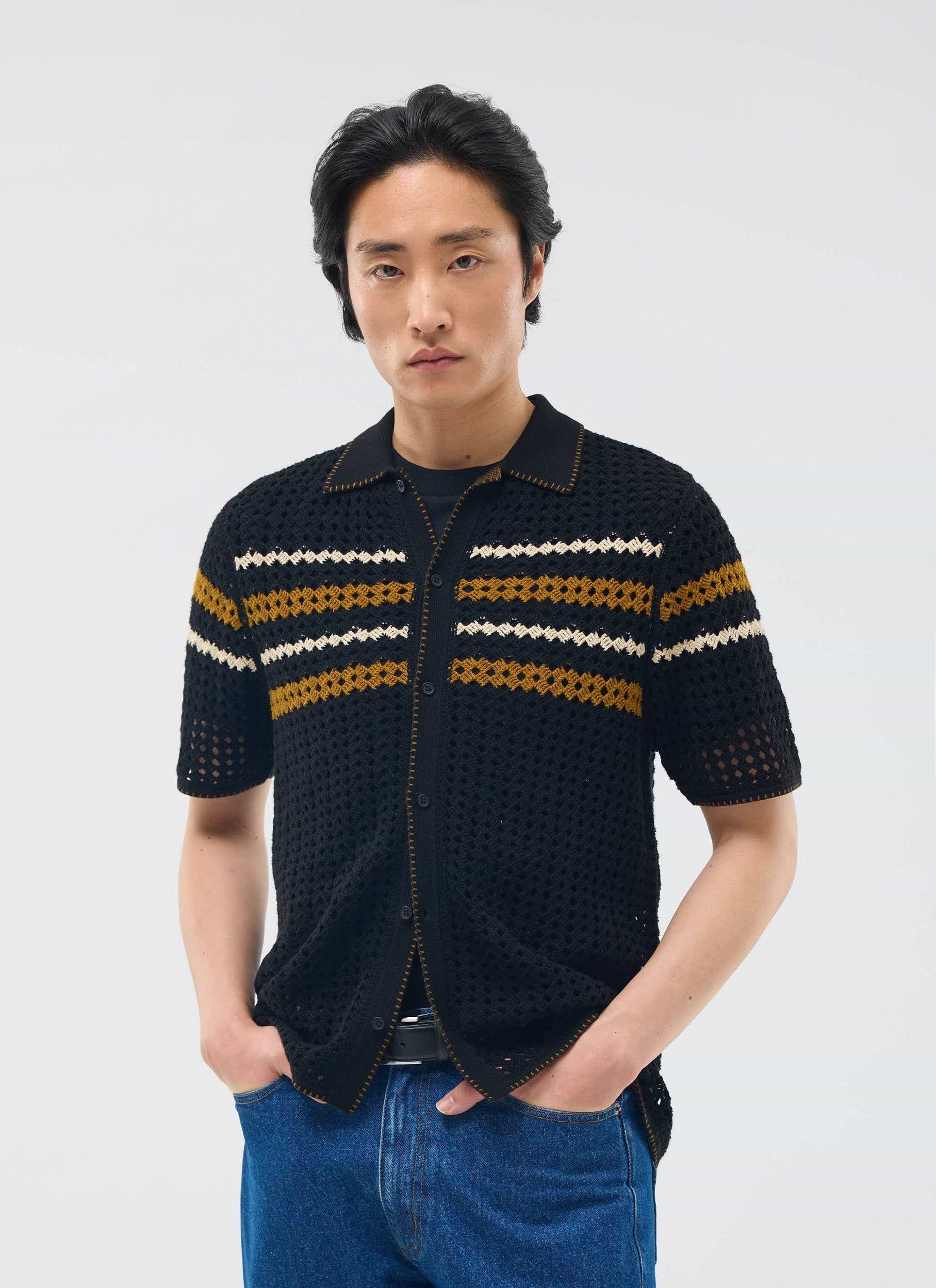 A model wears the Percival Pesaro Knitted Shirt in black, a crochet-style top with gold and white stripes across the chest.