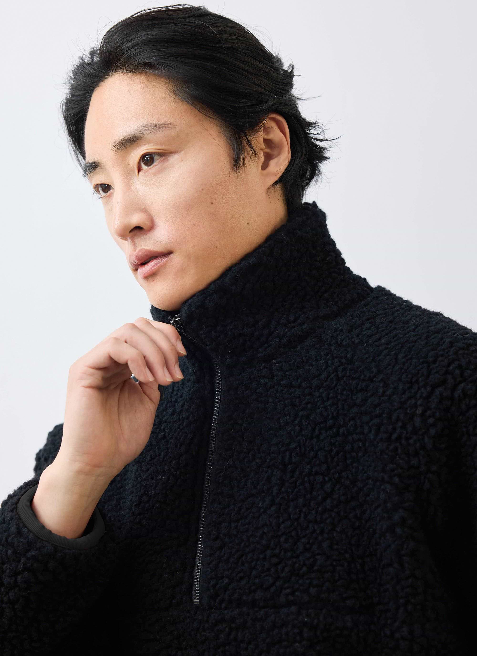 A close-up of a model wearing the black Percival Quarter Zip Wool Fleece Pullover, adjusting the high collar zip.