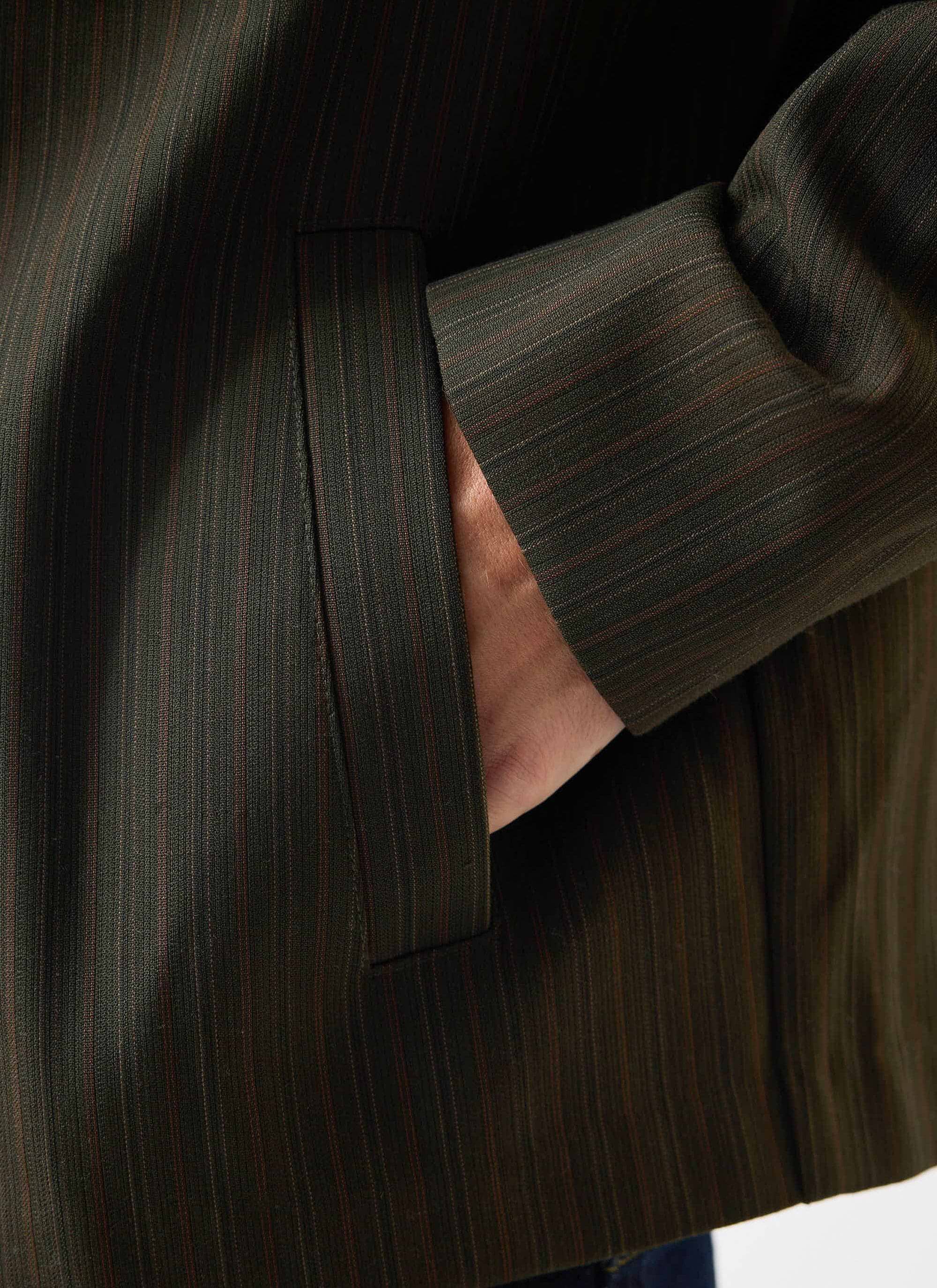 A close-up of the welt pocket and forest green pinstripe fabric on the Chapter Zip Up Jacket by Percival.