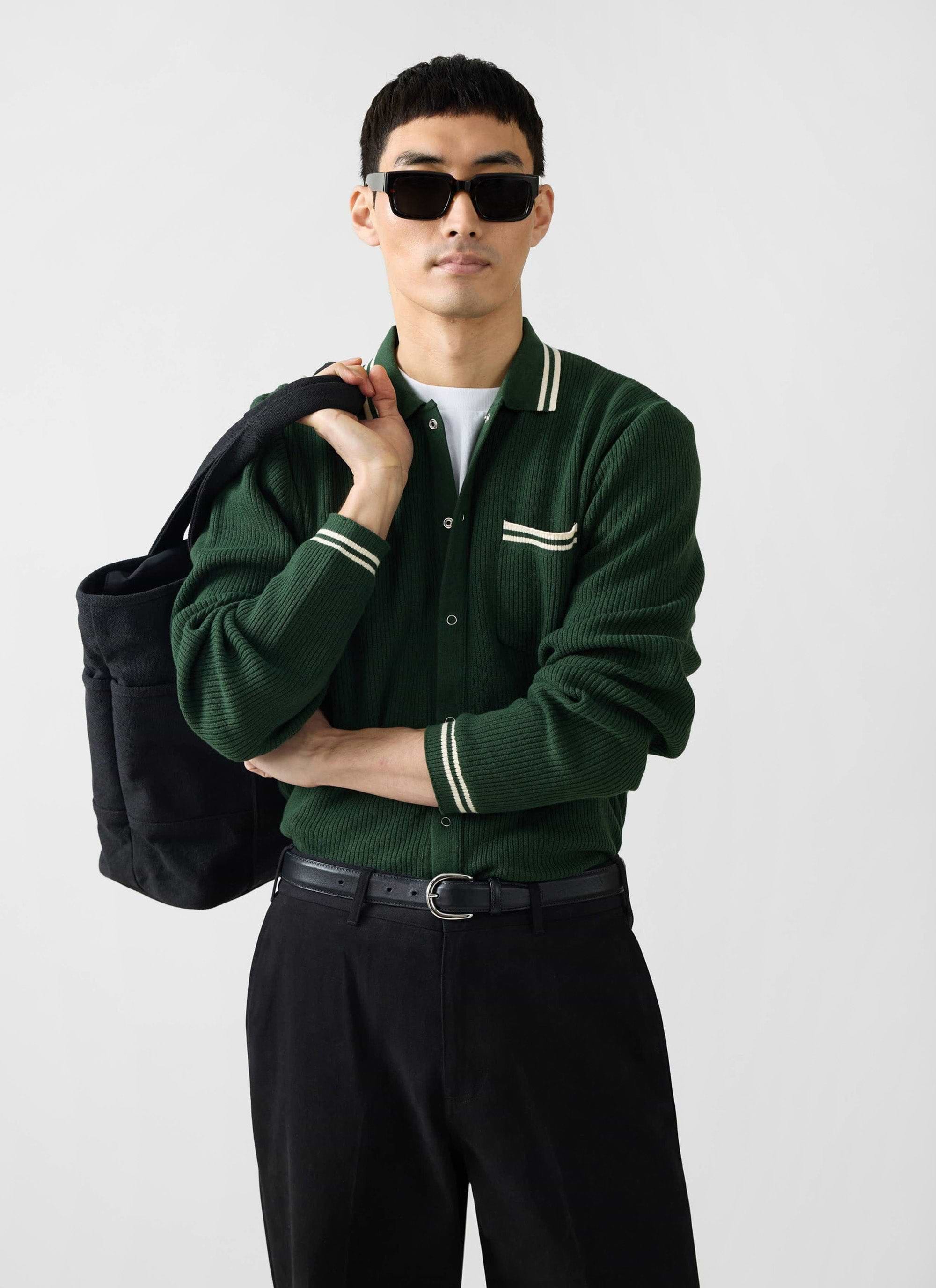 A model wears the Percival Pablo Cotton Knitted Shirt in forest green with black trousers, sunglasses and a black tote bag.