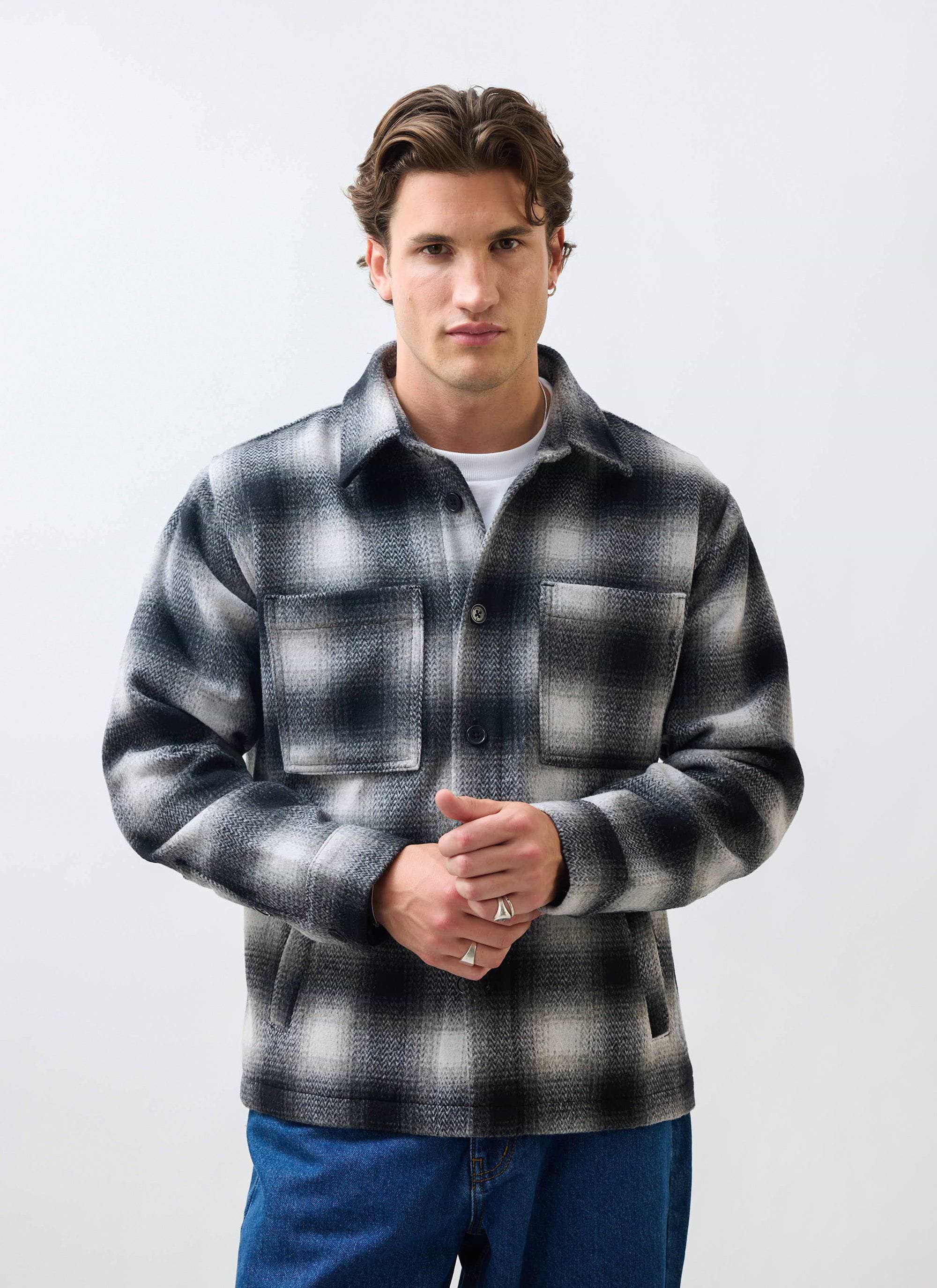 A male model wears the Percival Check Overshirt in a grey and black wool blend against a white studio background.