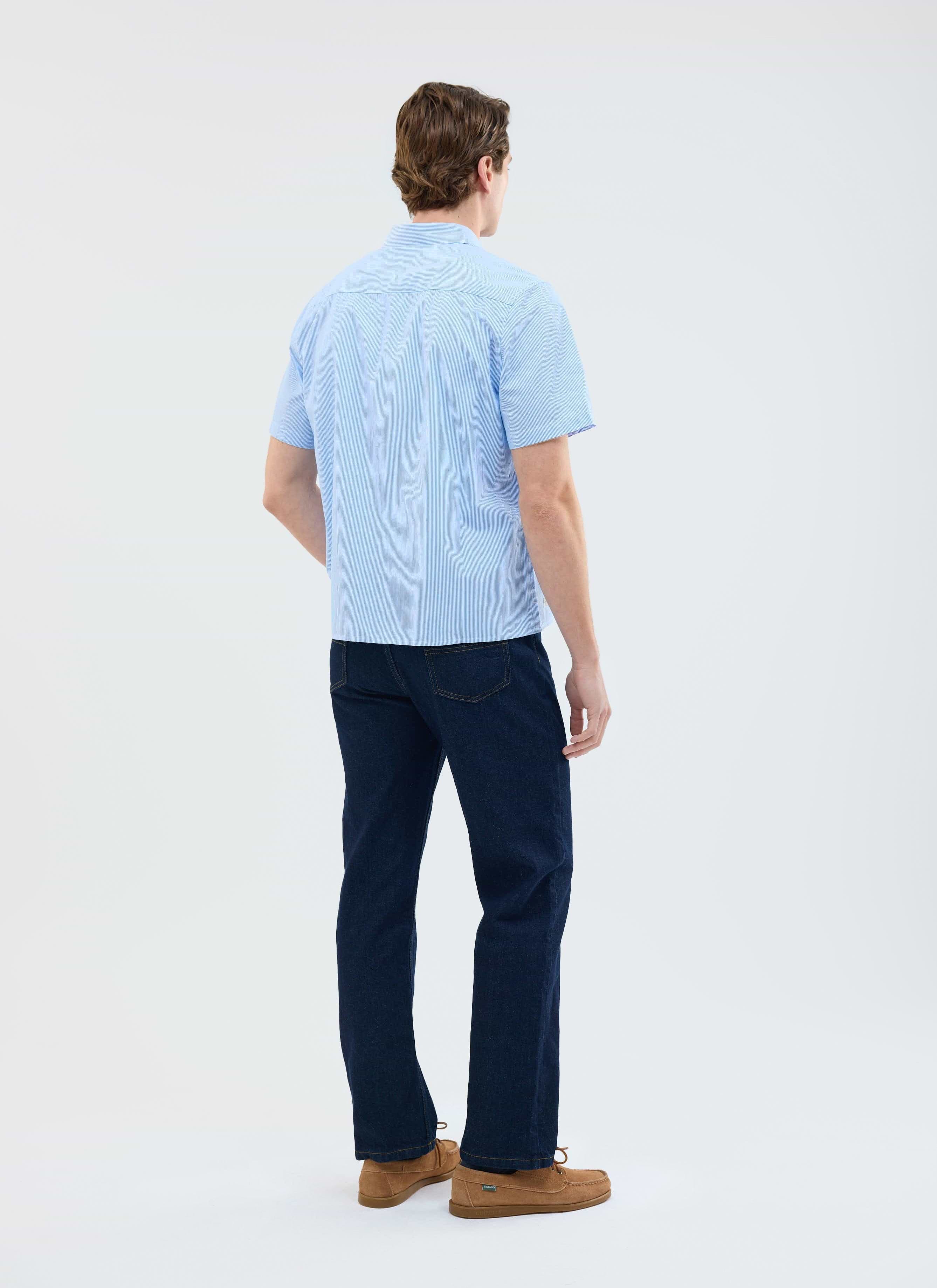 A model, viewed from behind, wears the Percival Sunflower Stripe Shirt in blue with dark denim and brown shoes.