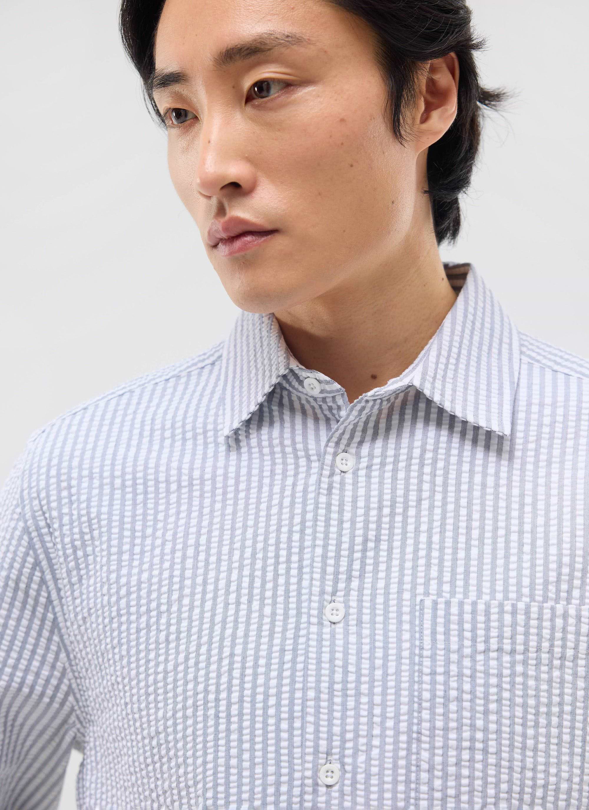 A close-up of a model wearing the Percival Seersucker Stripe Pearce Shirt in grey, highlighting its textured cotton fabric.