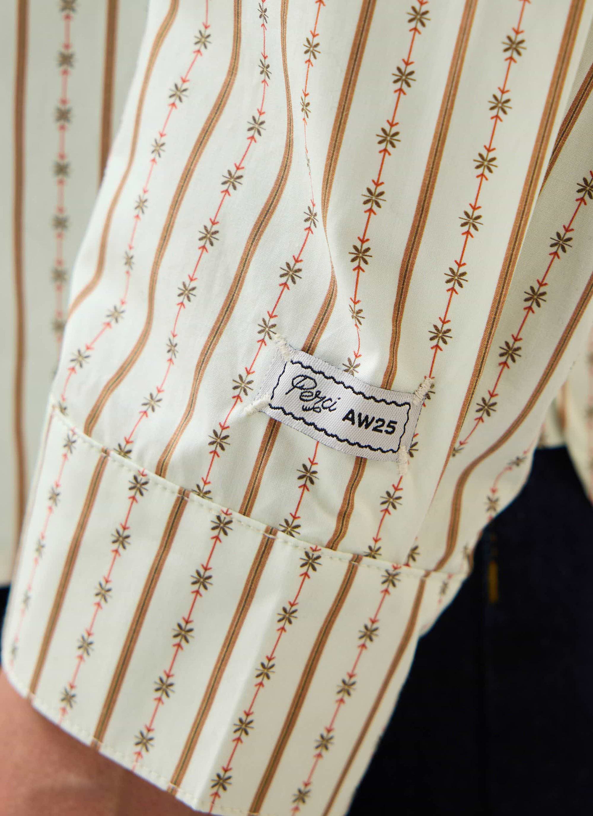 A close-up of the sleeve of the Percival Binding Oversized Pearce Shirt in ecru, showing the striped pattern and brand label.