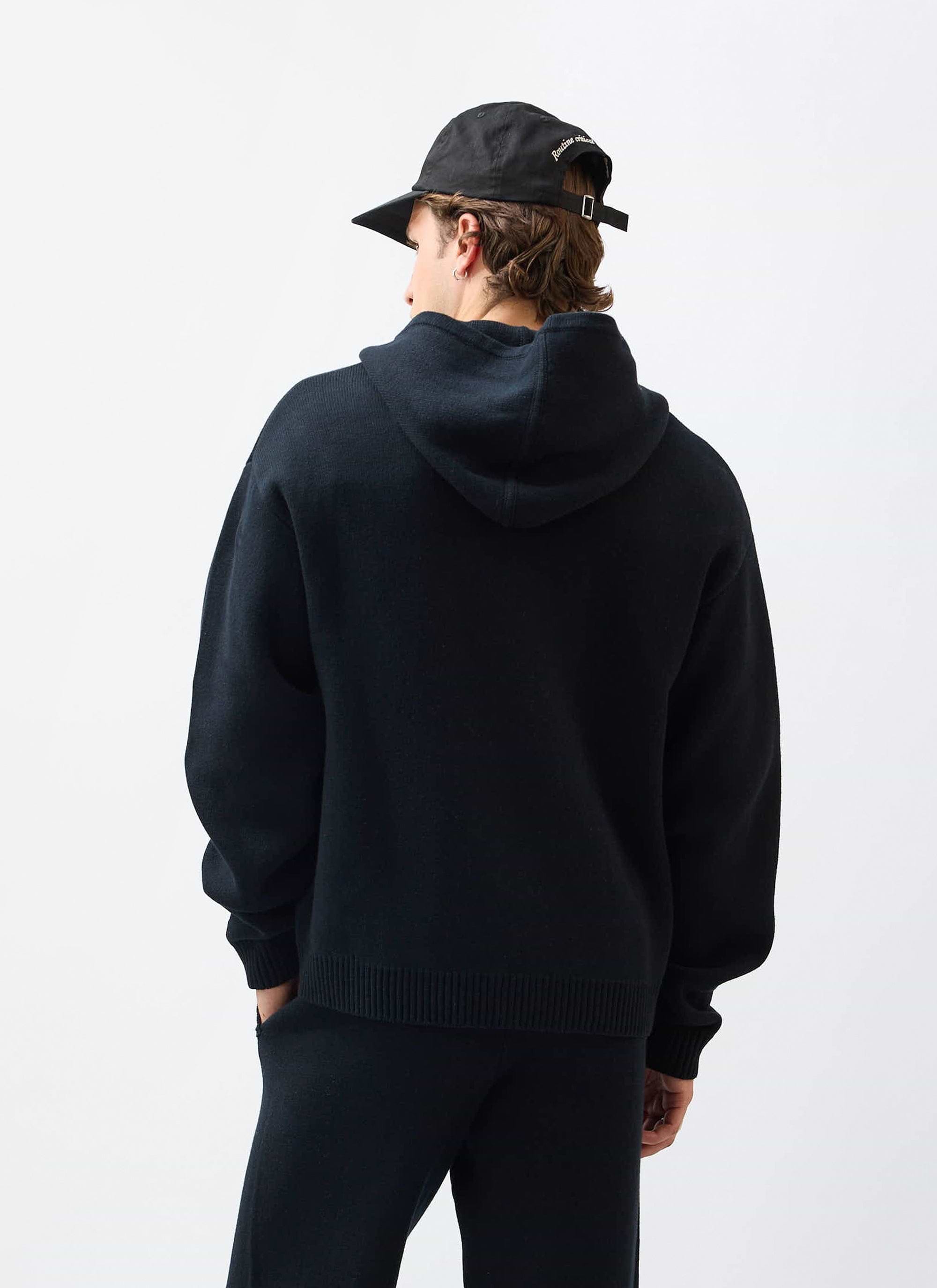 The back view of a model wearing the Percival Chronicle Knitted Hoodie in black, showing the oversized fit and hood.