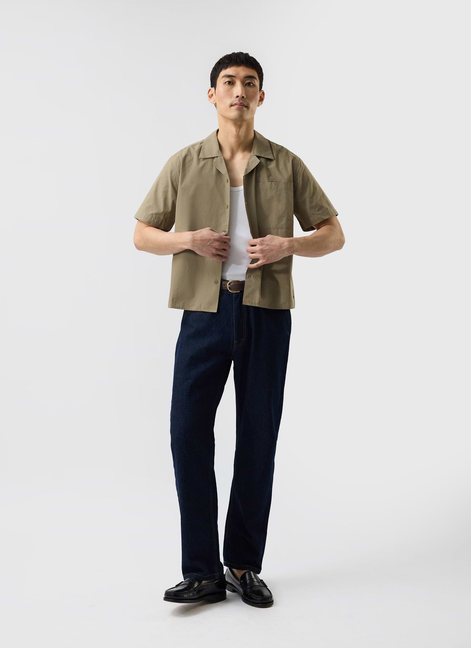 A male model wears the Percival Boxy Cropped Cuban Collar Shirt in olive, styled open over a white vest with dark jeans.