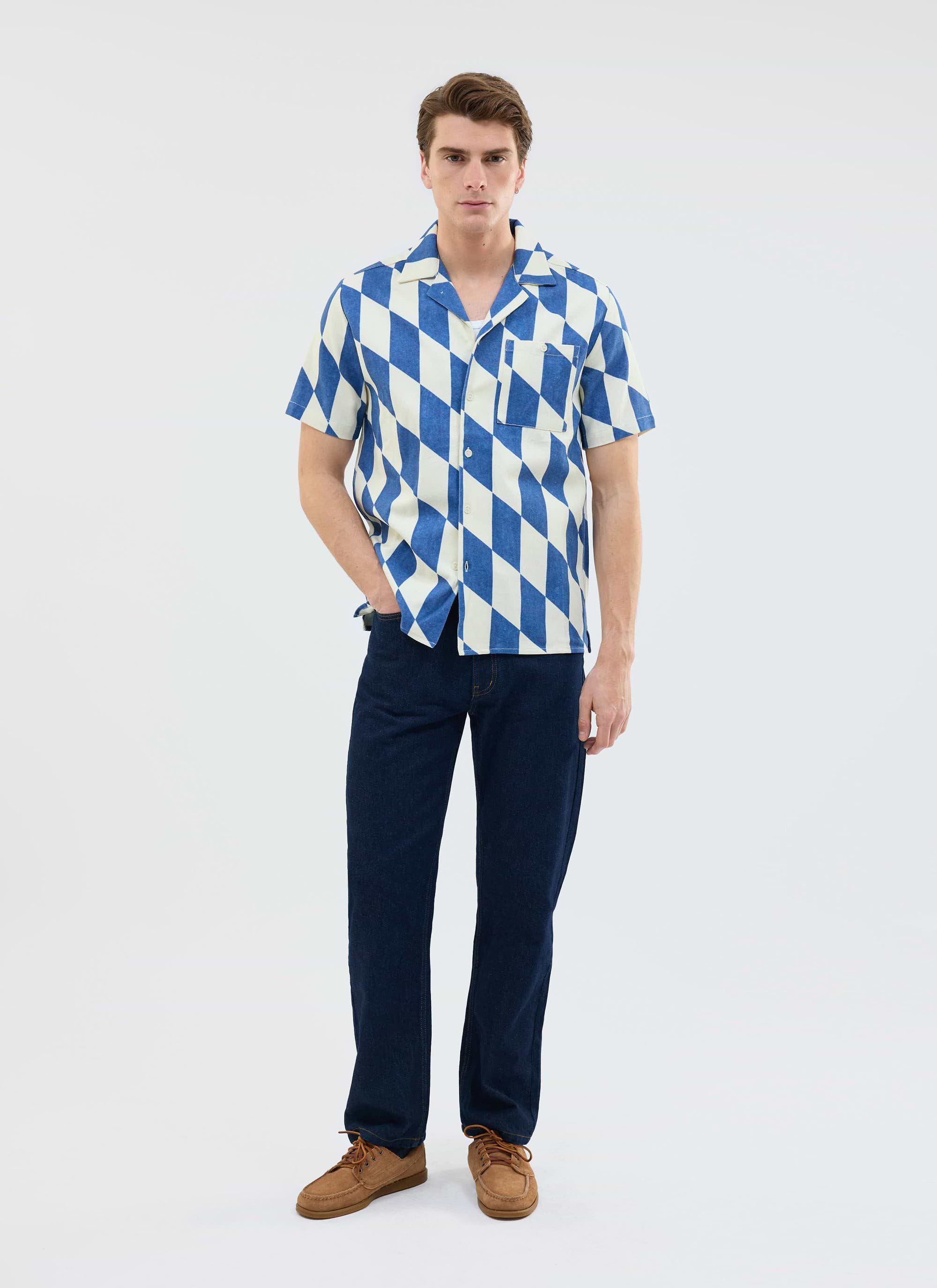 Model wears the Percival Market Diamond Cuban Shirt in ecru and navy, styled with dark jeans and brown shoes.