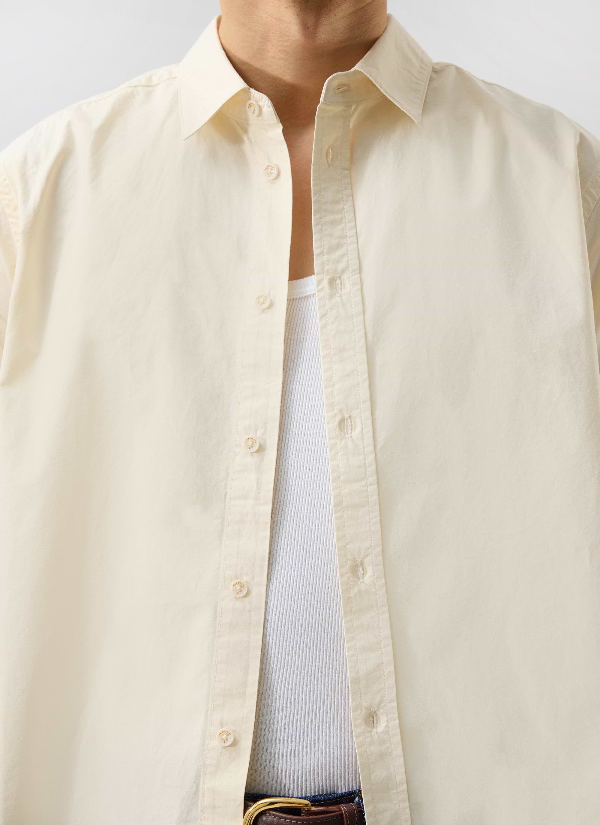 Close up of a model wearing the Percival Boxy Cropped Clerk Shirt in ecru, styled open over a white vest.