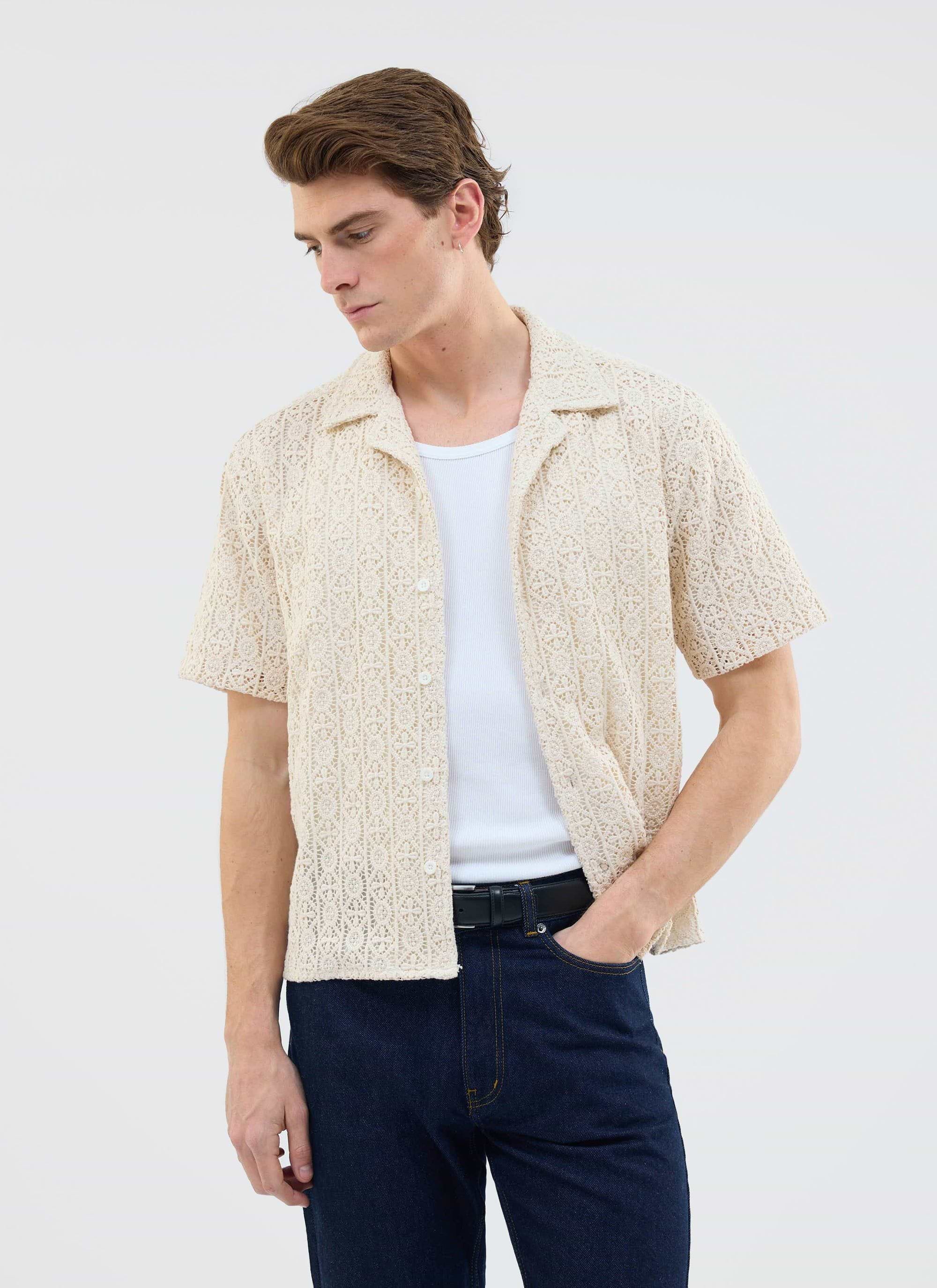 A model wears the Percival Elio Crochet Cuban Shirt in ecru, layered over a white vest with dark blue jeans.