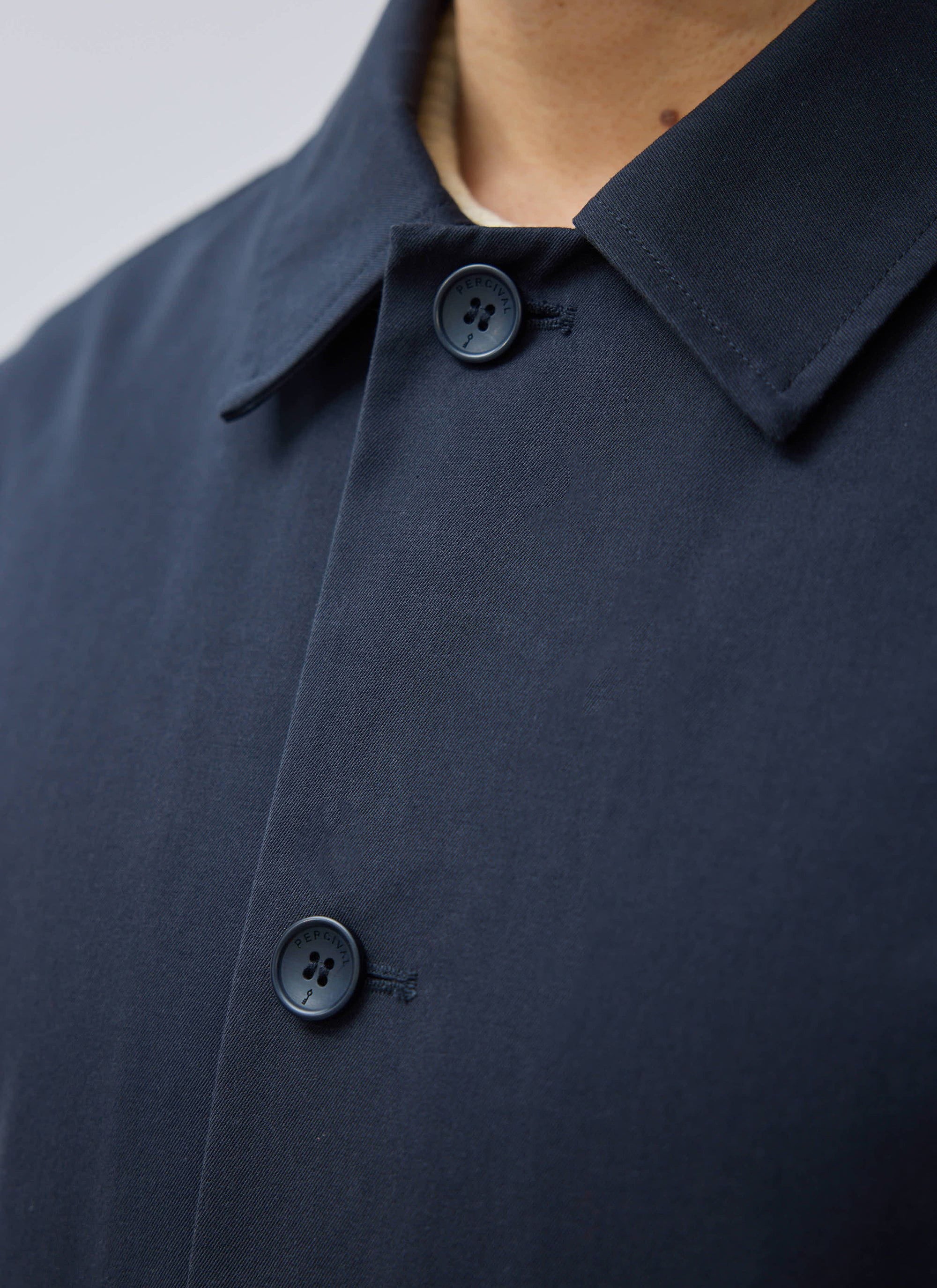 Close-up of the navy Sherlock Short Trench Coat by Percival, showing the branded buttons and waterproof technical fabric.