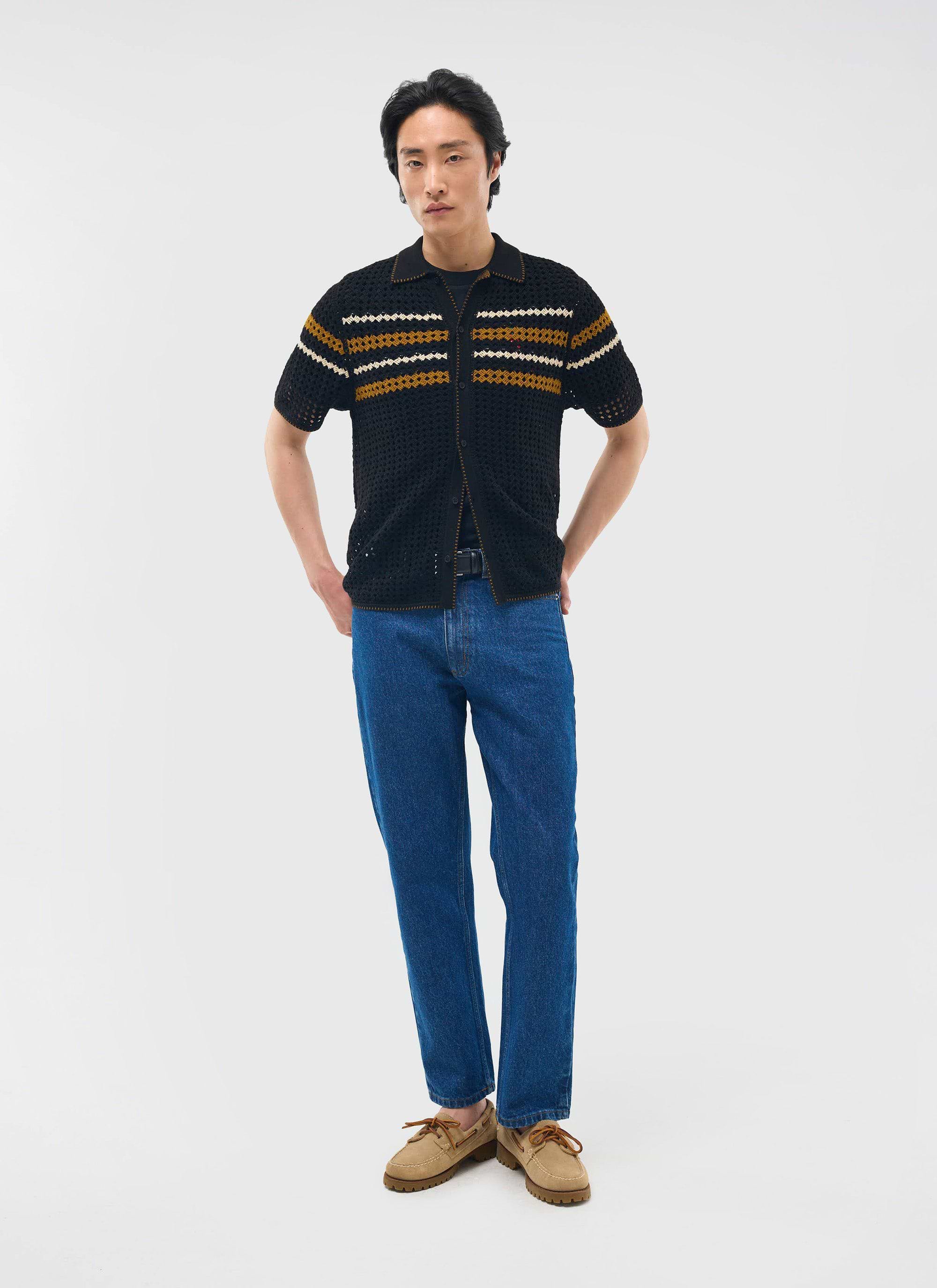 A model wears the black Percival Pesaro Knitted Shirt, a crochet design with stripes, styled with blue jeans.