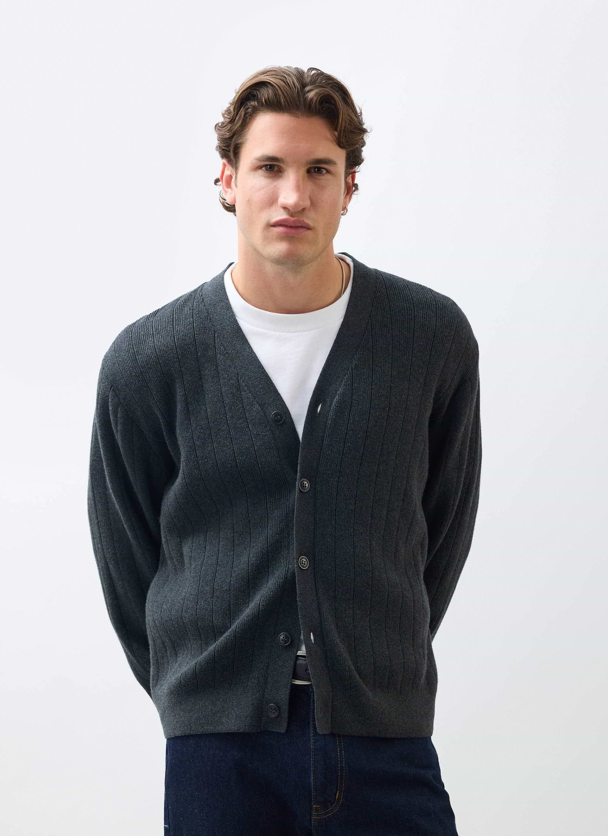 A model wears the Percival Editor Cardigan in dark charcoal grey, styled over a white t-shirt against a plain background.