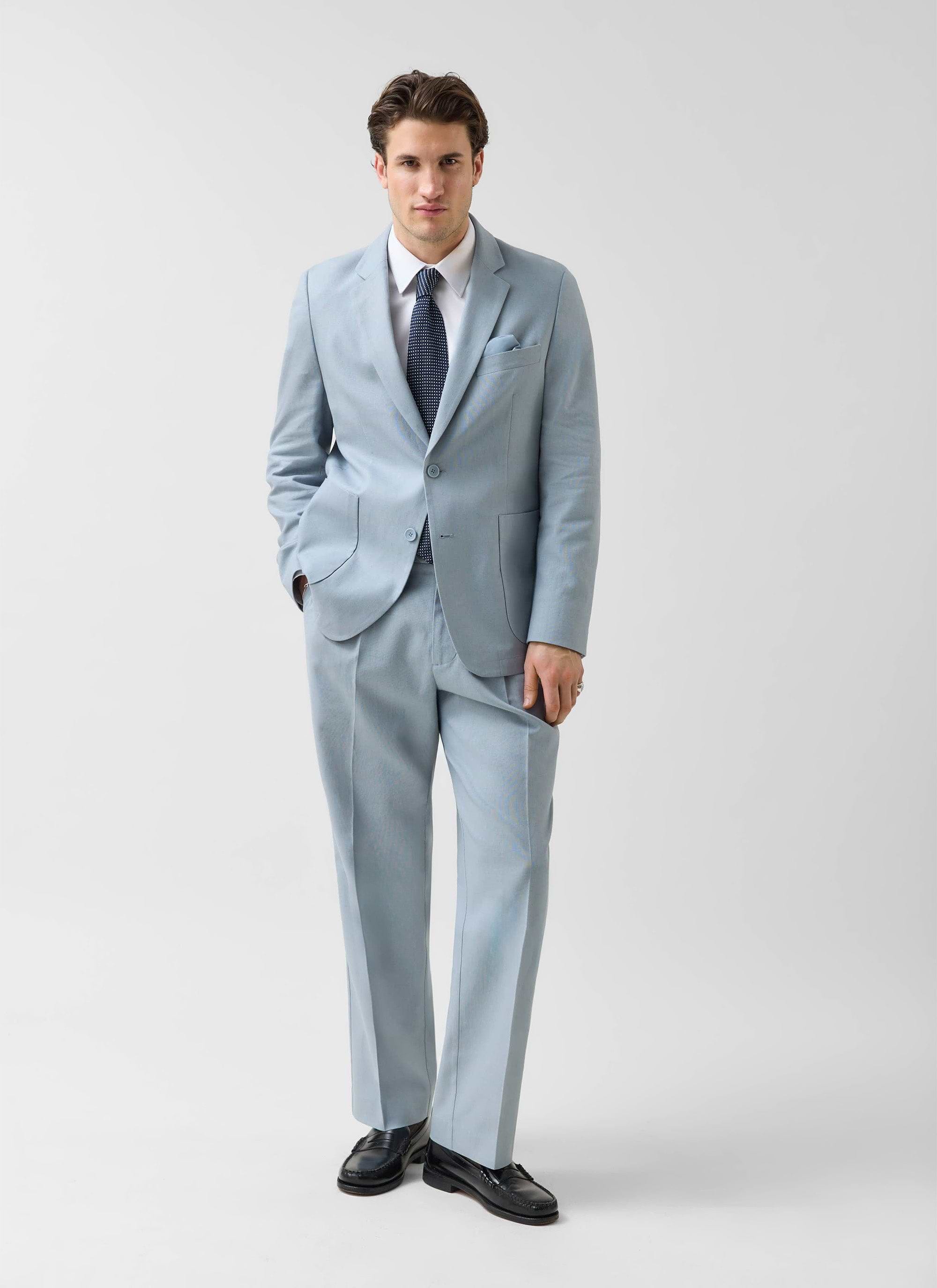 A man models the Percival light blue tailored linen blazer with matching trousers, a white shirt and a navy tie.