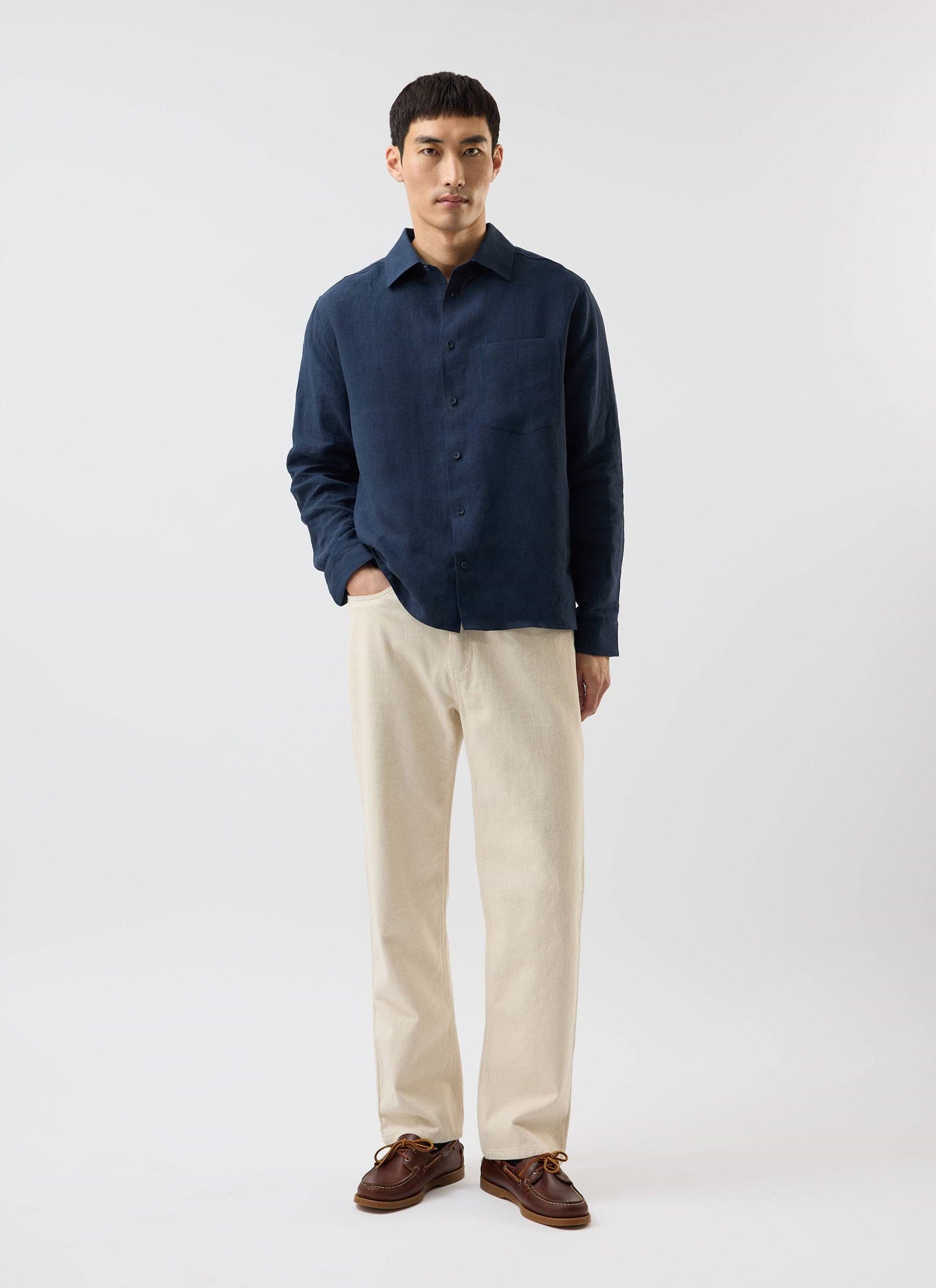 A model wears the navy linen Pearce Shirt from Percival, paired with cream trousers and brown boat shoes in a studio.
