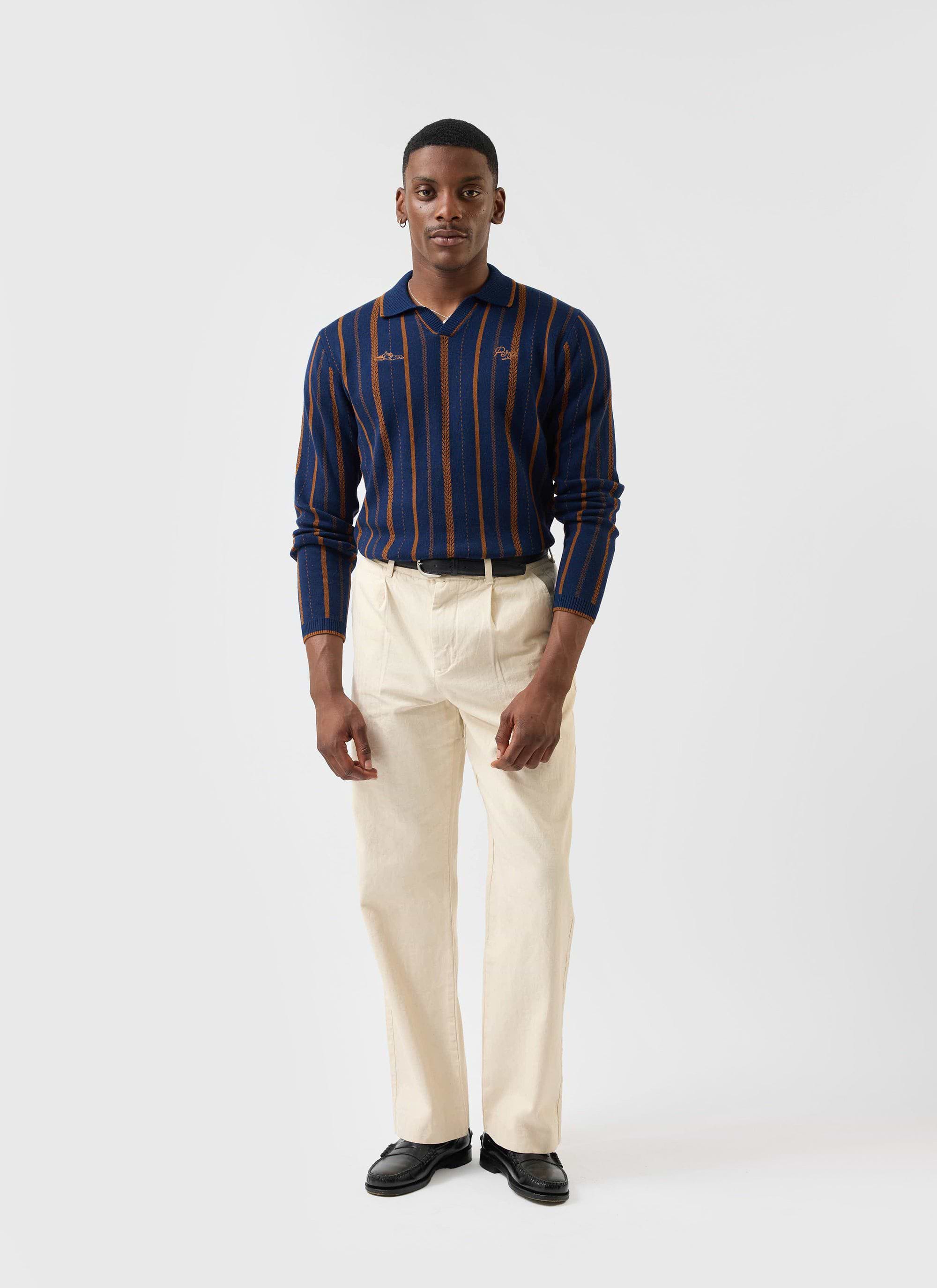 A model wears the navy striped Percival Citation Knitted Football Shirt, styled with cream trousers and black loafers.