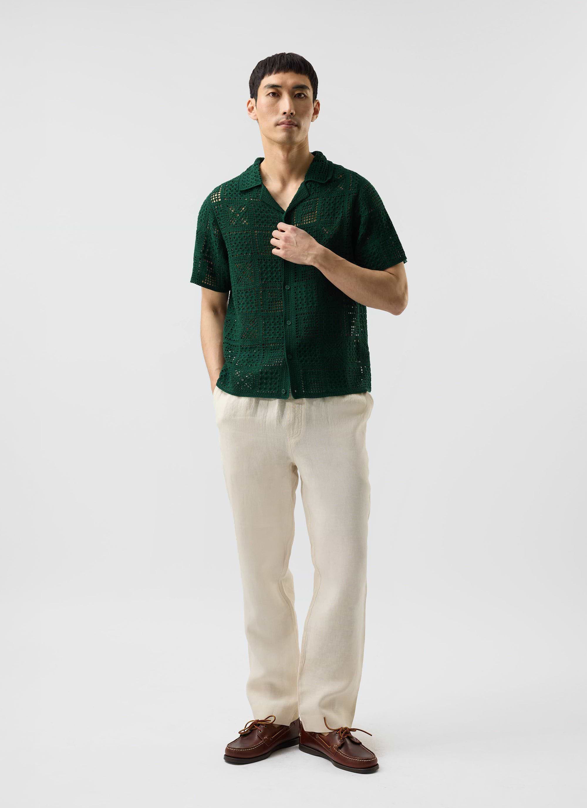 A model styles the Percival Crochet Groundsman Shirt in forest green, paired with cream linen trousers and brown boat shoes.