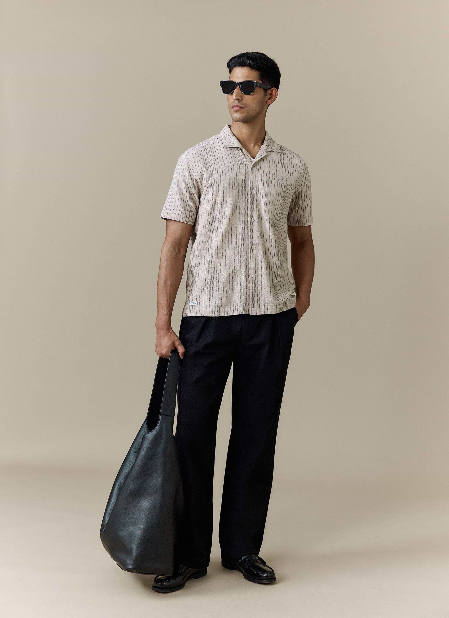 Percival Leland Cuban Shirt in cream textured cotton, styled with black trousers, sunglasses and a black leather tote bag.