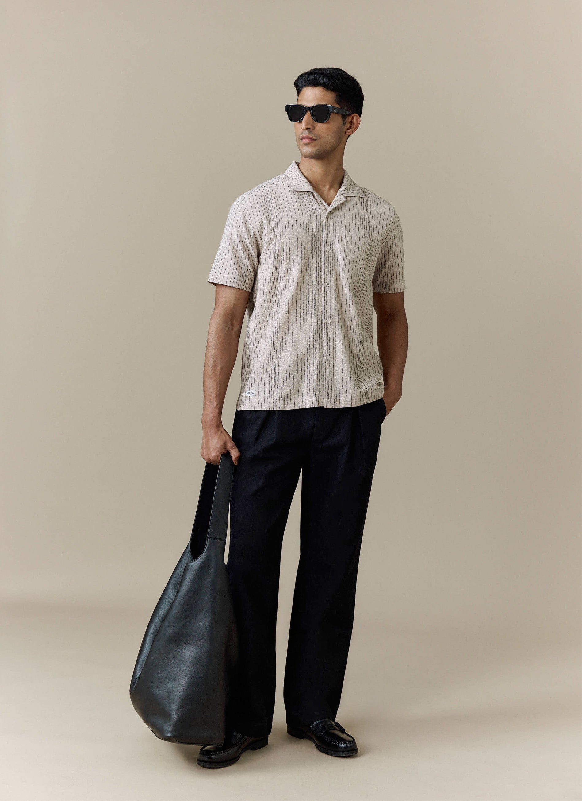 Percival Leland Cuban Shirt in cream textured cotton, styled with black trousers, sunglasses and a black leather tote bag.