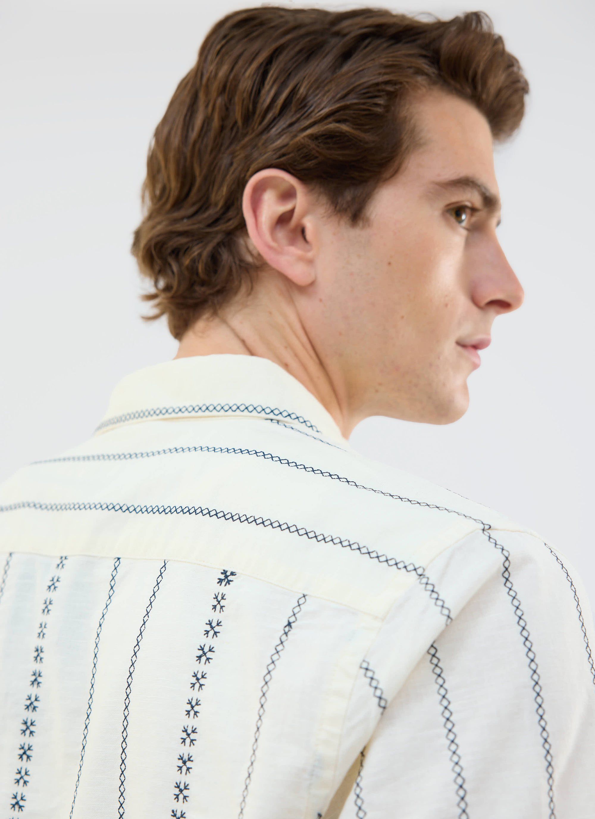A close-up of the back of a model wearing the Percival Cross Stitch Boxy Clerk Shirt in ecru, showing the blue embroidery.
