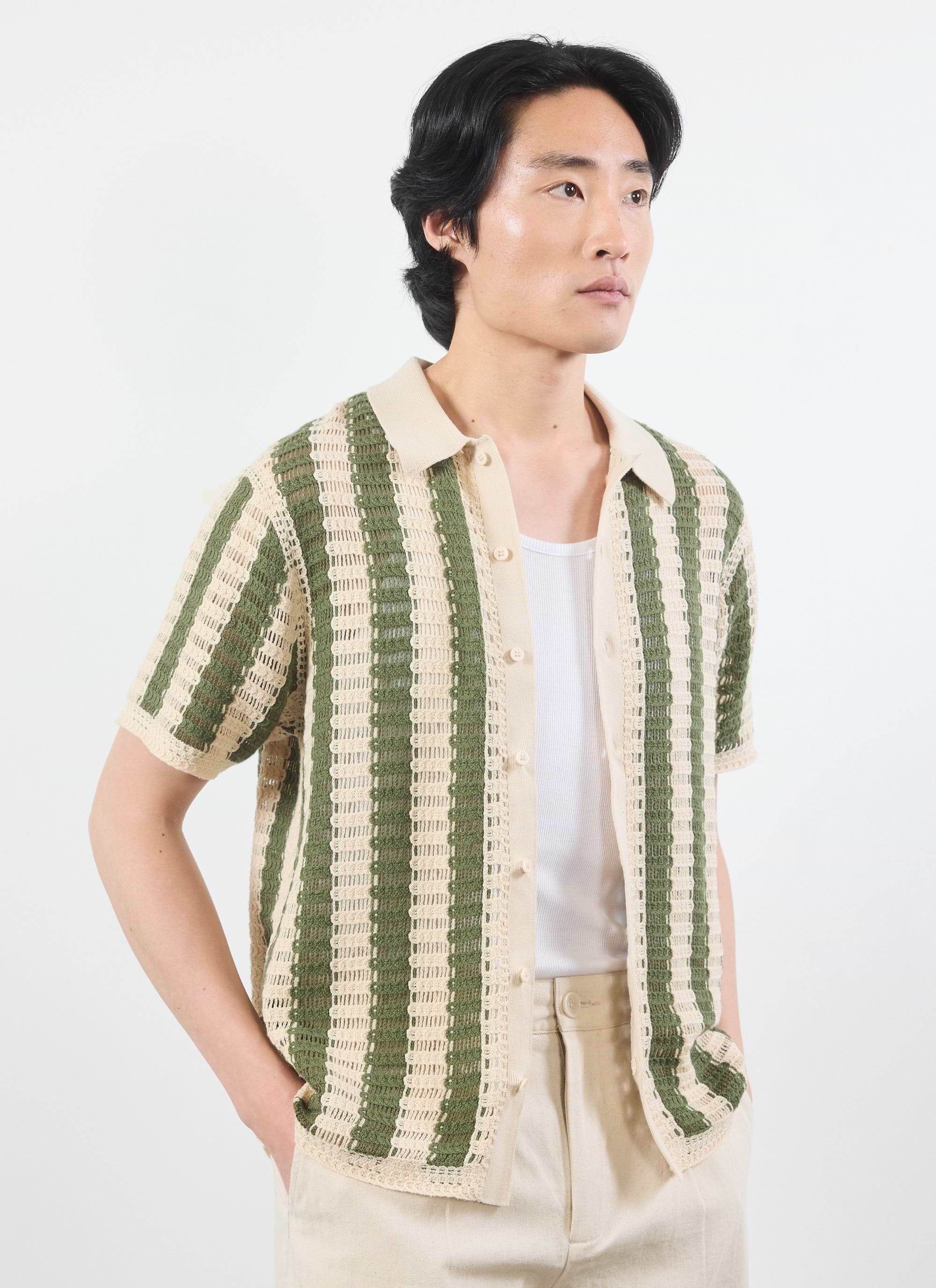 A model wears the Percival Barletta Knitted Shirt in olive, a striped crochet design, styled open over a white vest.