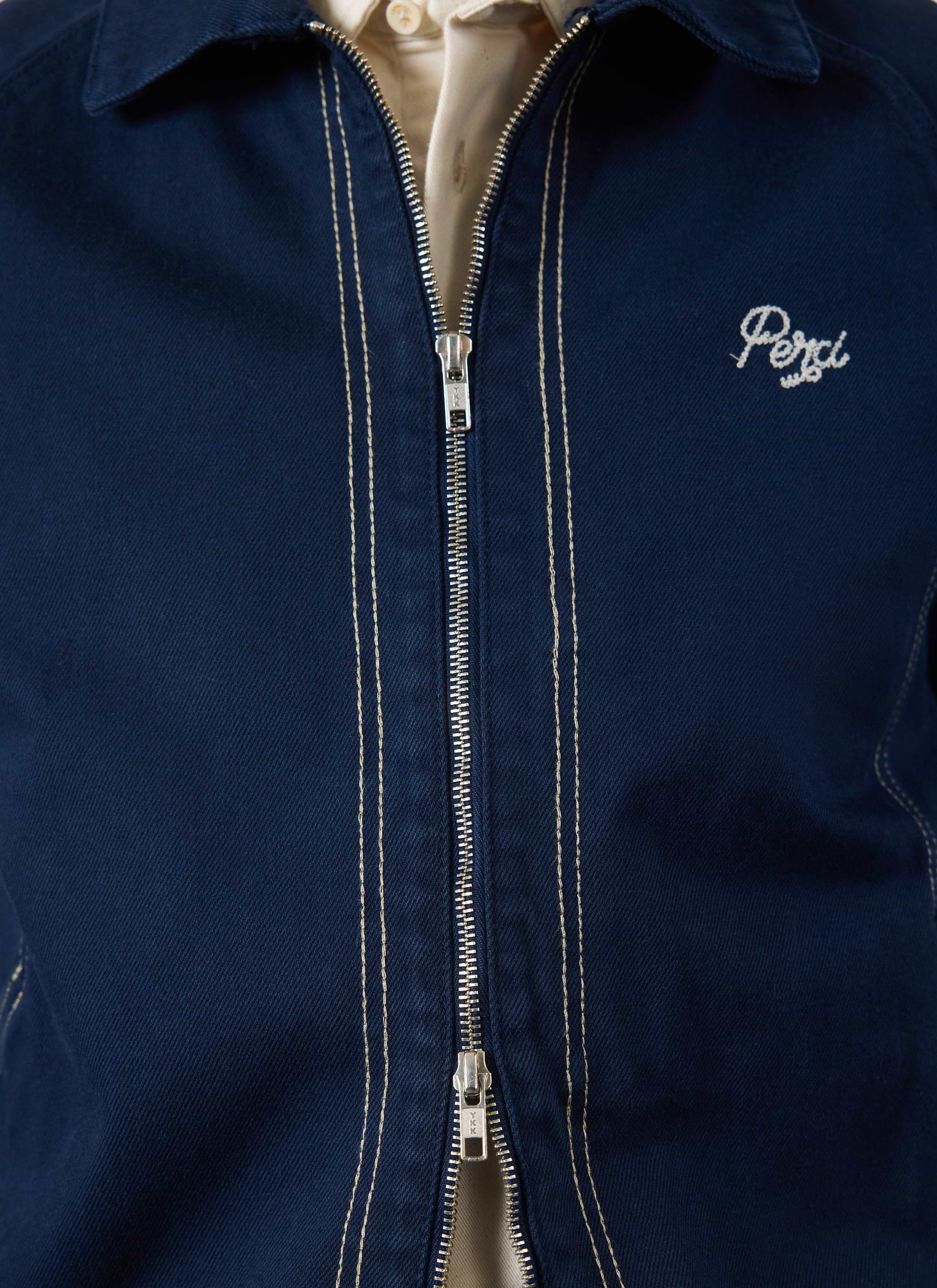 A close-up of the navy Calabria Harrington Jacket by Percival, showing the zip, contrast stitching, and 'Perci' logo.