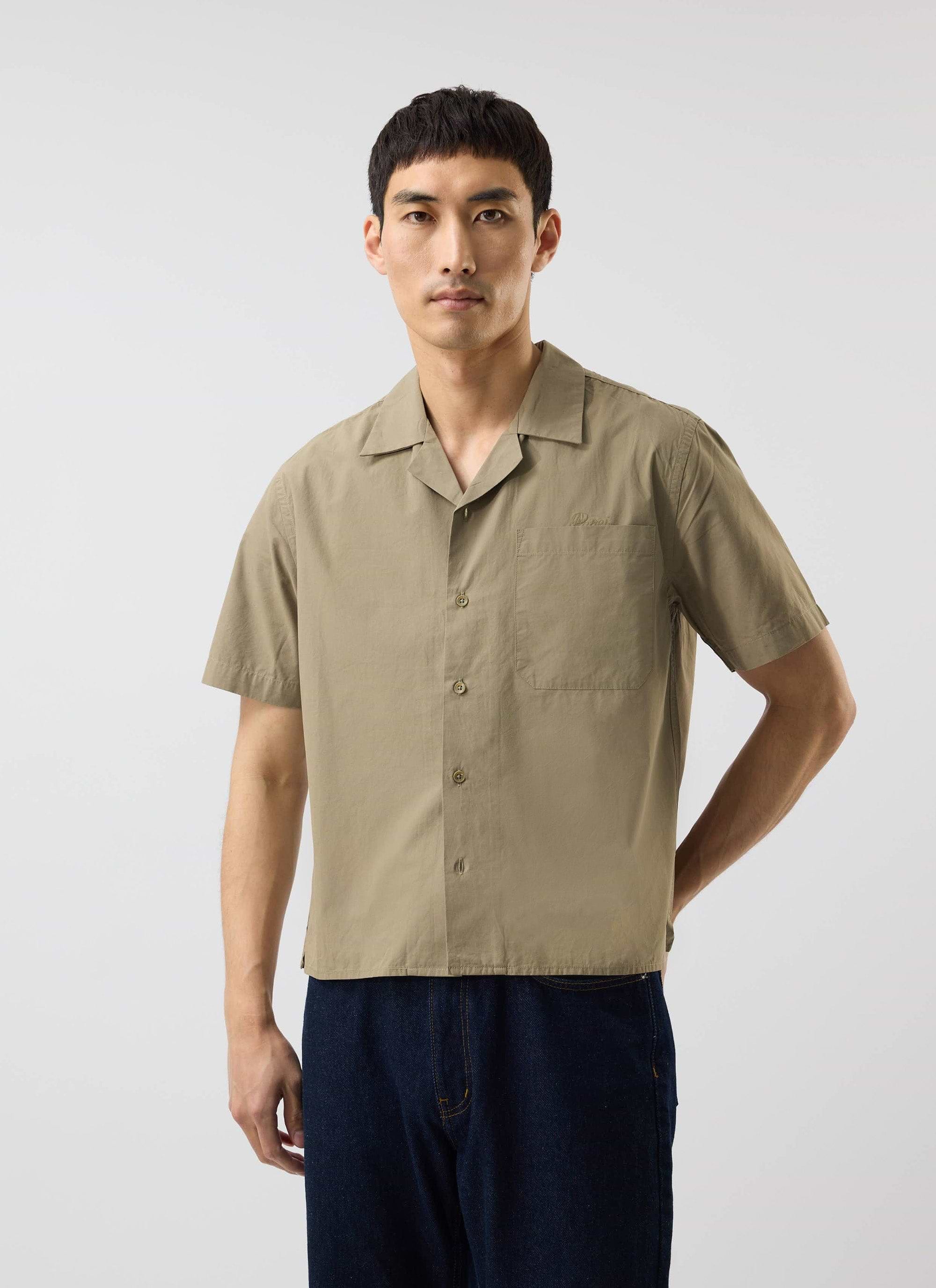 A studio shot of a man wearing the Percival boxy fit Cuban collar shirt in olive green, paired with dark wash jeans.