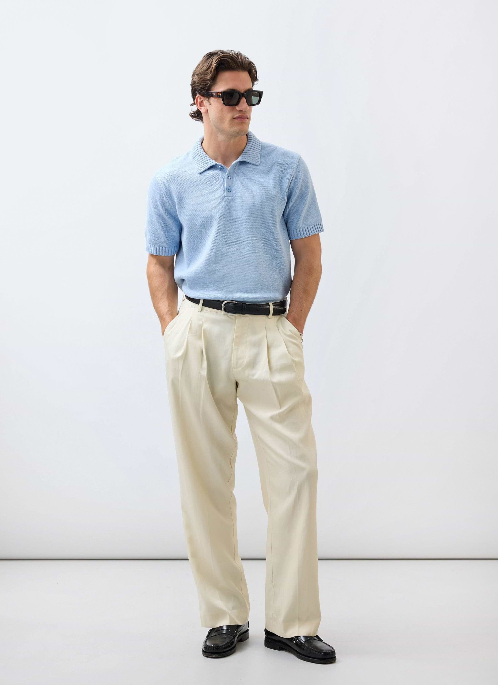 A model wears the Percival Verso Short Sleeve Knitted Shirt in heather blue, styled with cream trousers and sunglasses.