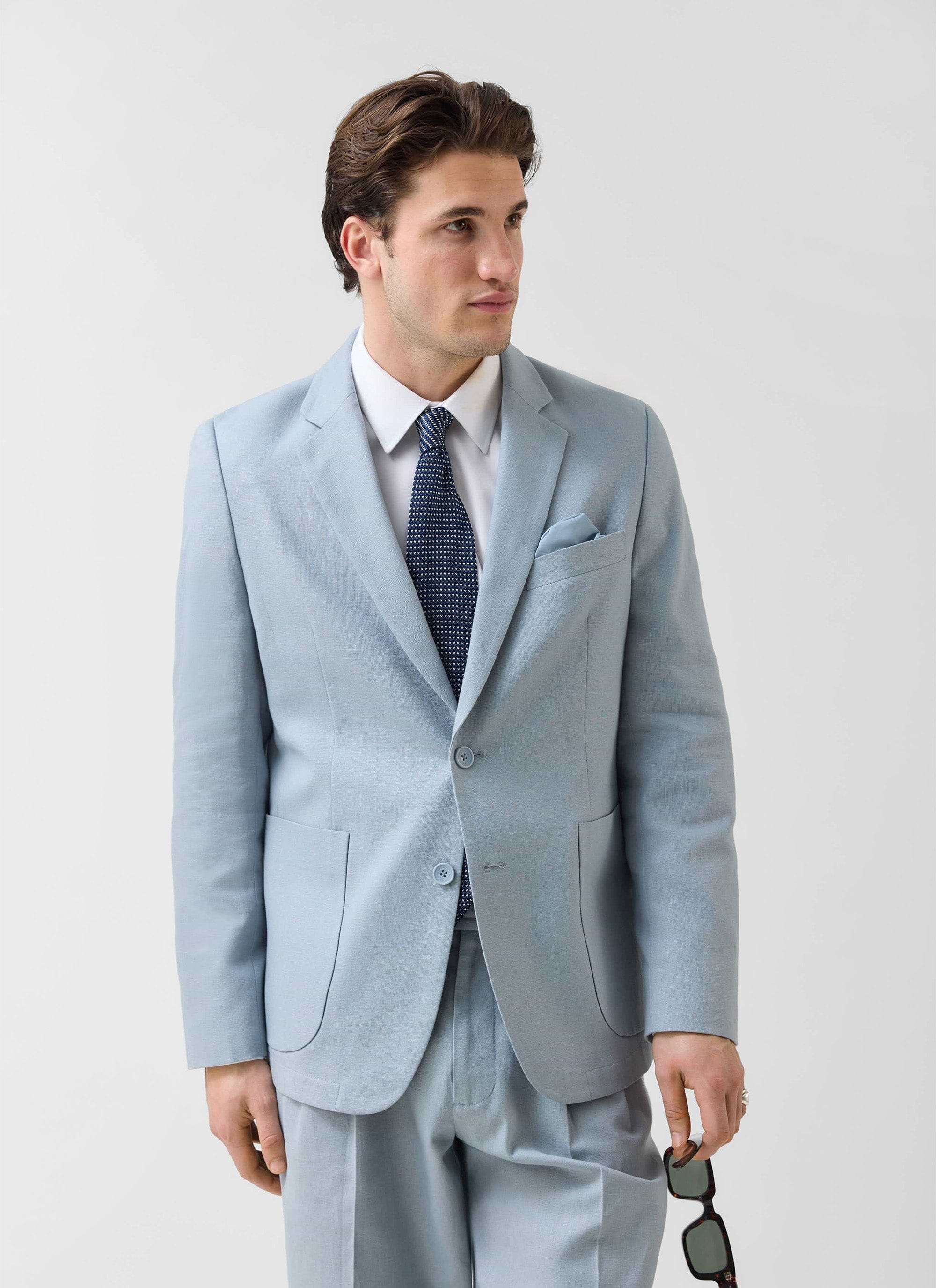 A model wears the Percival light blue tailored linen blazer with a white shirt, tie and matching trousers.