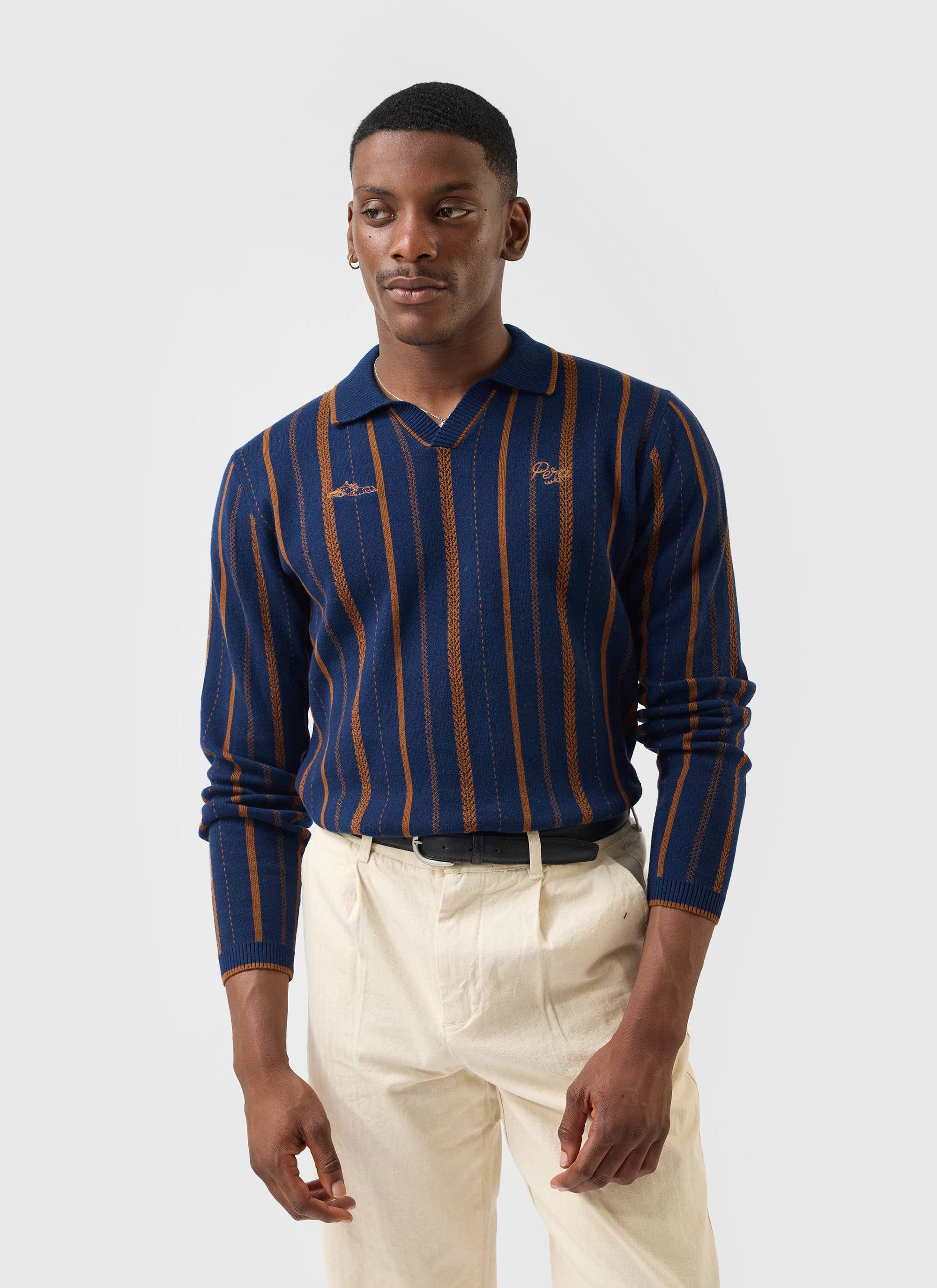 A model wears the Percival Citation Knitted Football Shirt in navy with brown vertical stripes, paired with cream trousers.