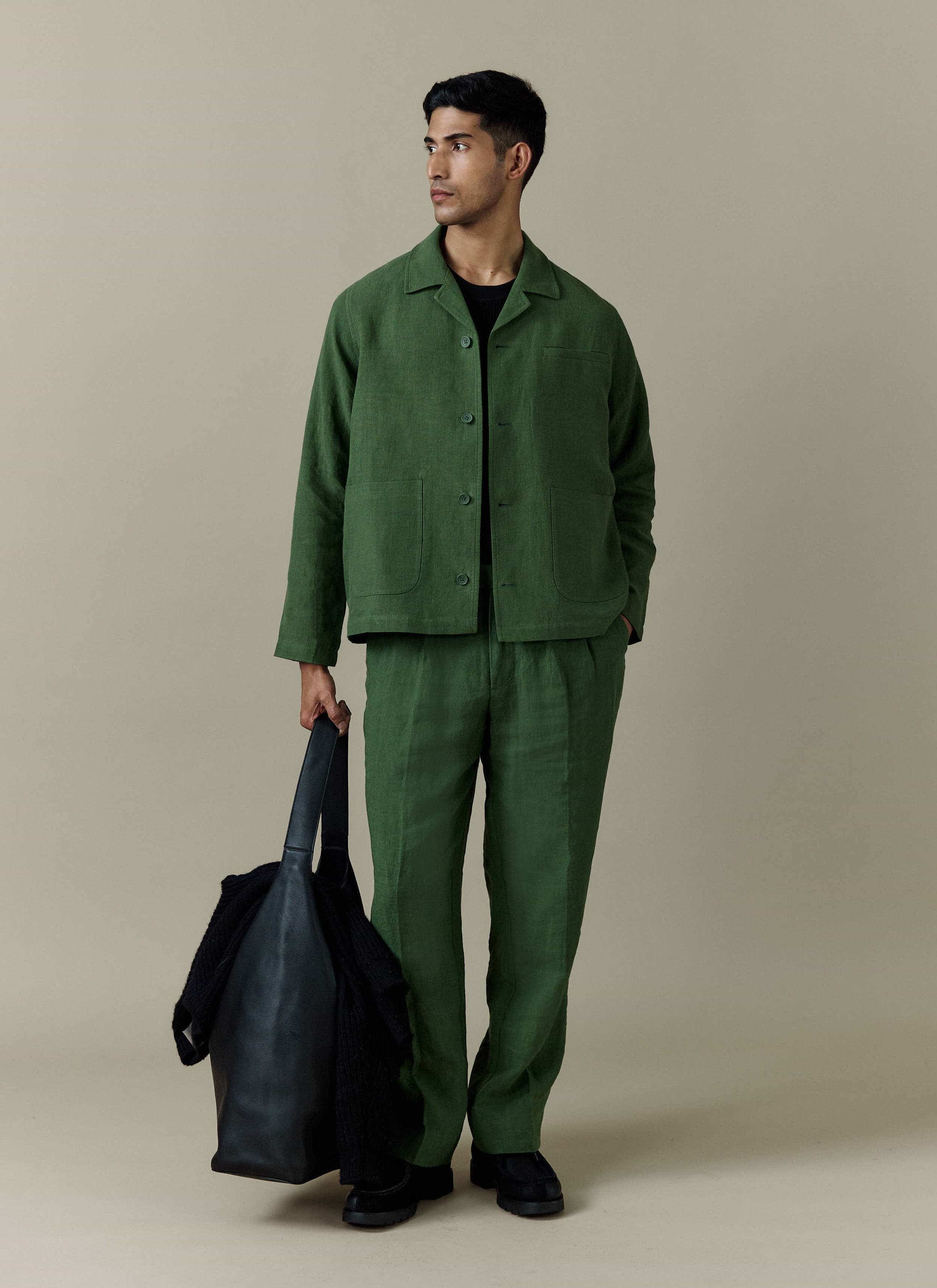 A model wears the Percival forest green linen overshirt with matching trousers, holding a black tote bag.