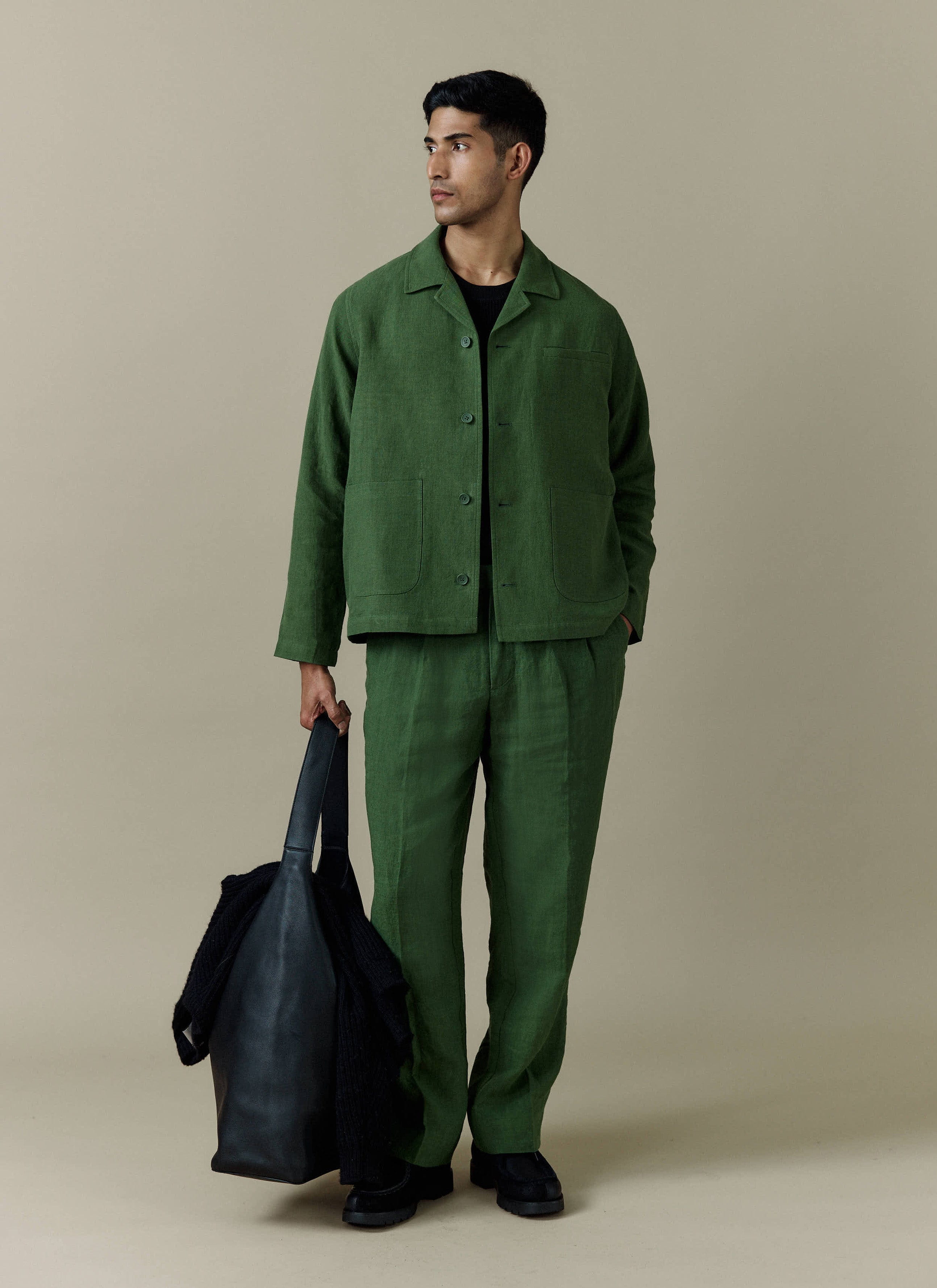 A model wears the Percival forest green linen overshirt with matching trousers, holding a black tote bag.