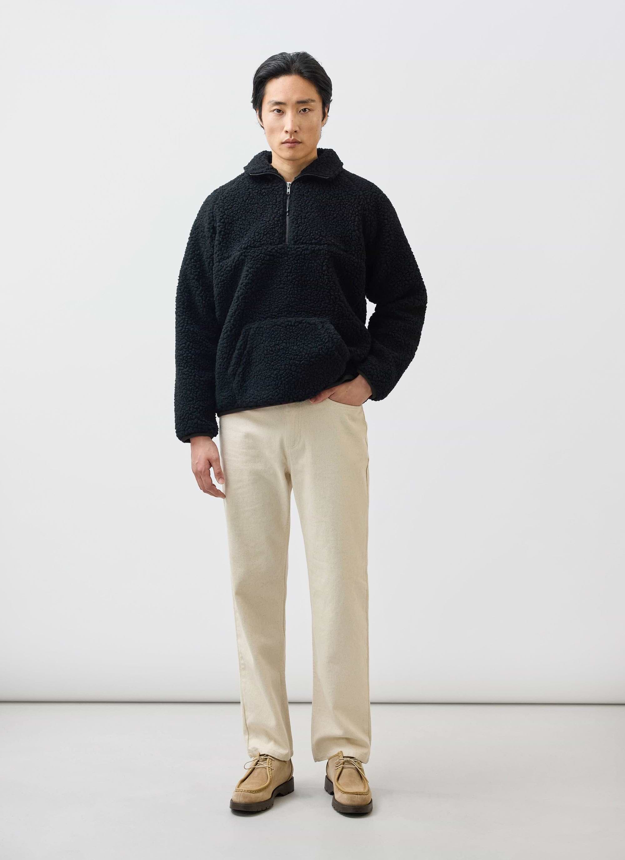 A model wears the black Quarter Zip Wool Fleece Pullover from Percival with cream trousers against a white background.