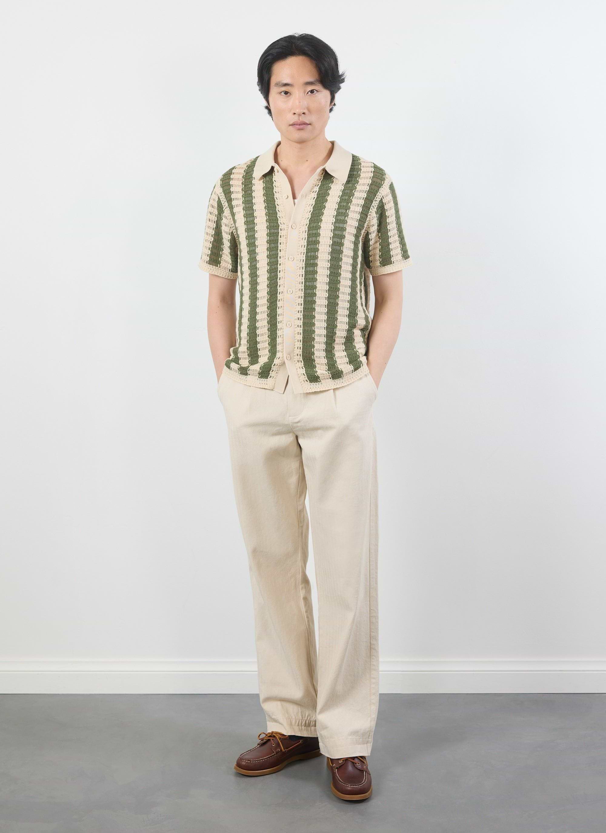 A model wears the Percival Barletta Knitted Shirt in olive, a striped crochet top, styled with cream trousers.
